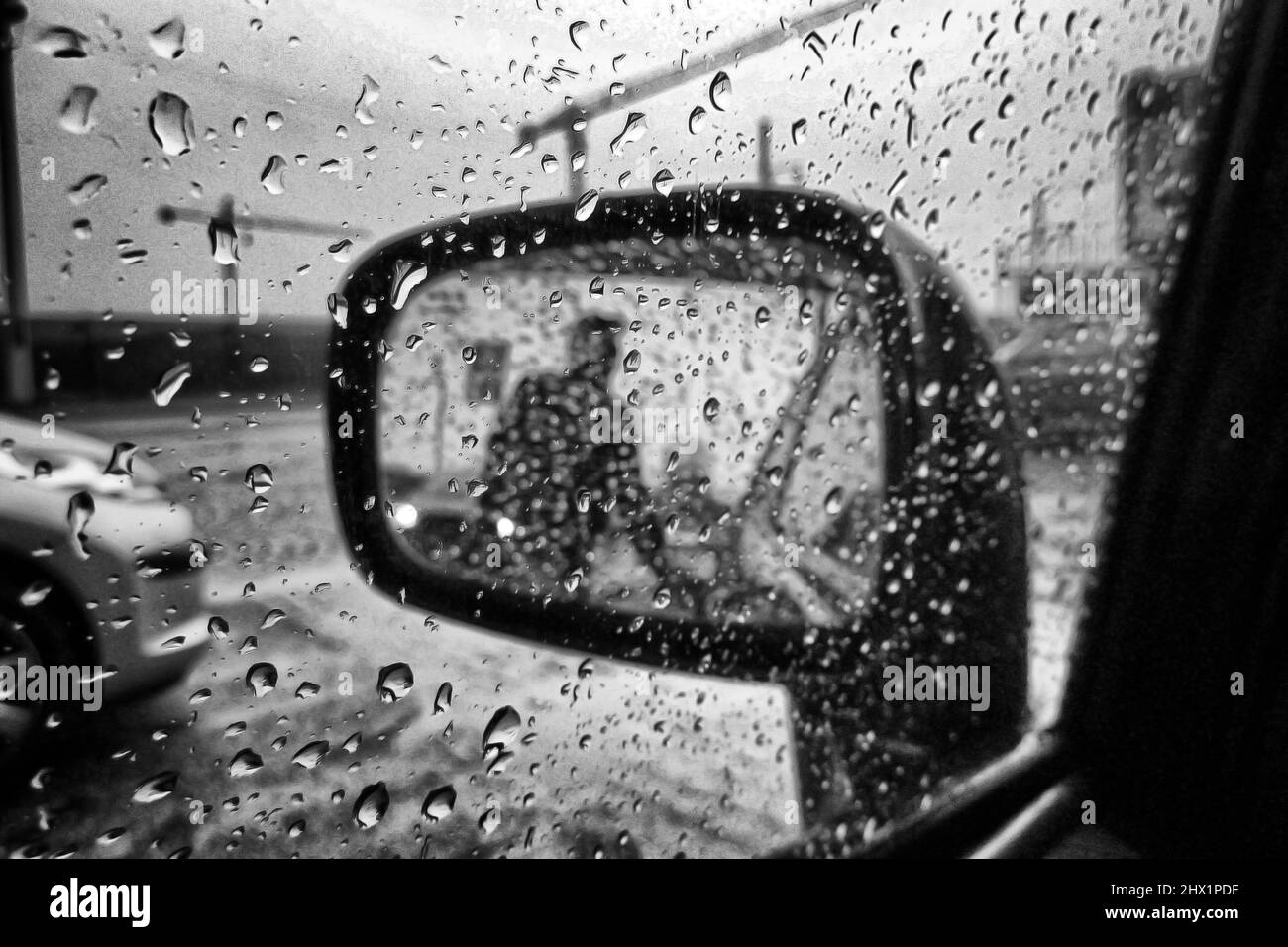 Tankpumpenwärter durch Regentropfen Nasser Rückspiegel - Auto- und transportbezogene Schwarzweißfotografie in Fine Art Stockfoto