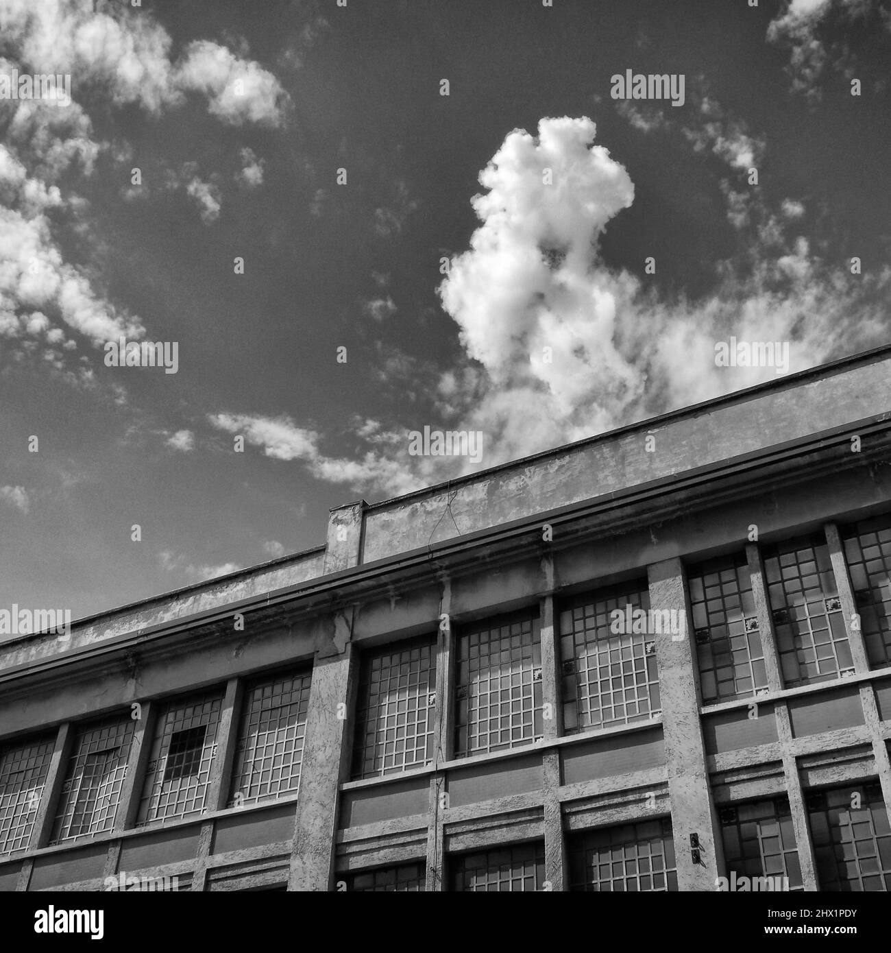 Monochromatische Kunstfotografie eines industriellen Altbaus mit weißen Wolken am Himmel Stockfoto
