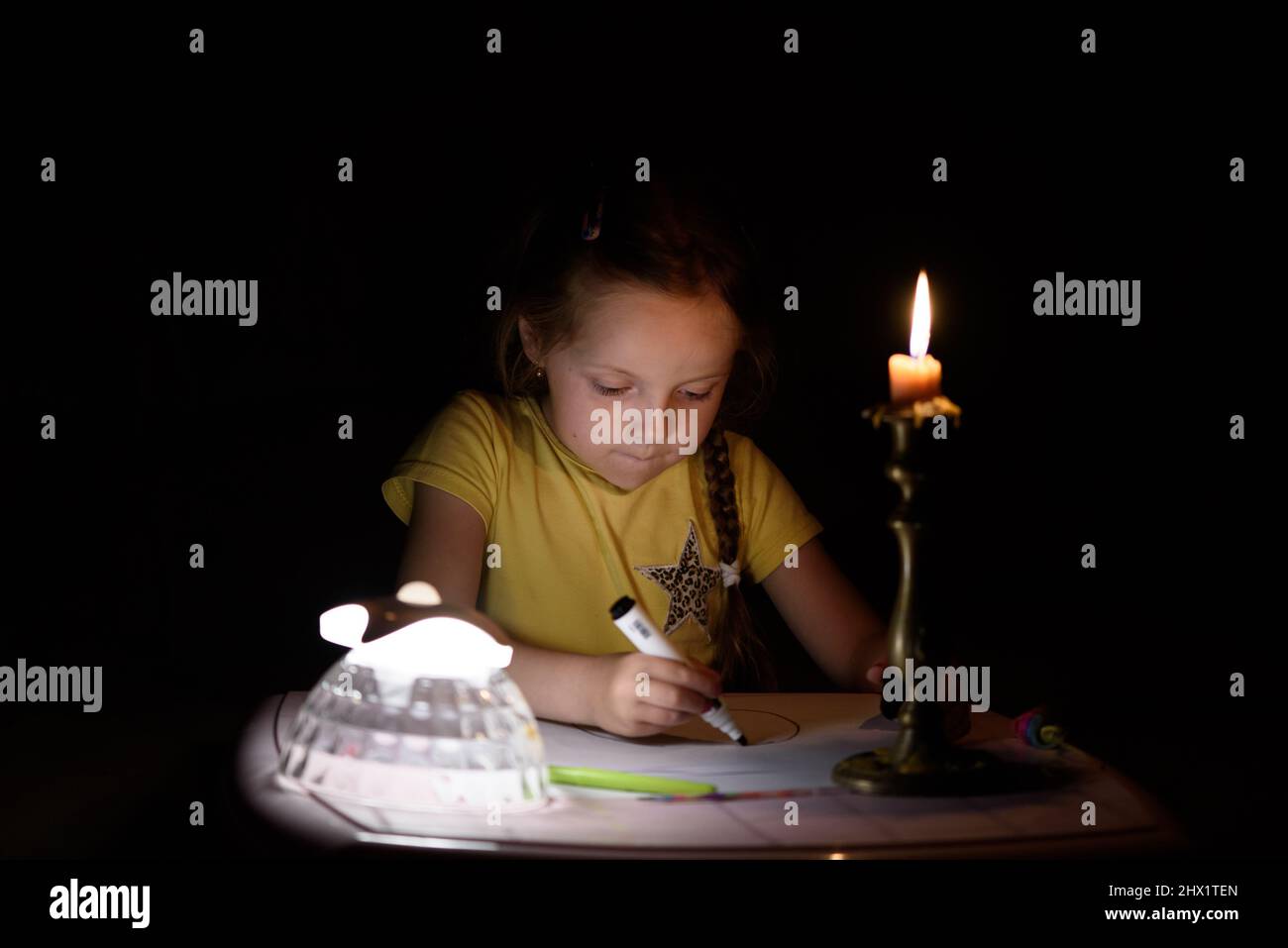 Das kleine Mädchen zieht in einem dunklen Raum Fantasiefiguren in die Nähe von Kerzen. Kind, das während eines Stromausfalls seine Lieblingssache macht. Stockfoto