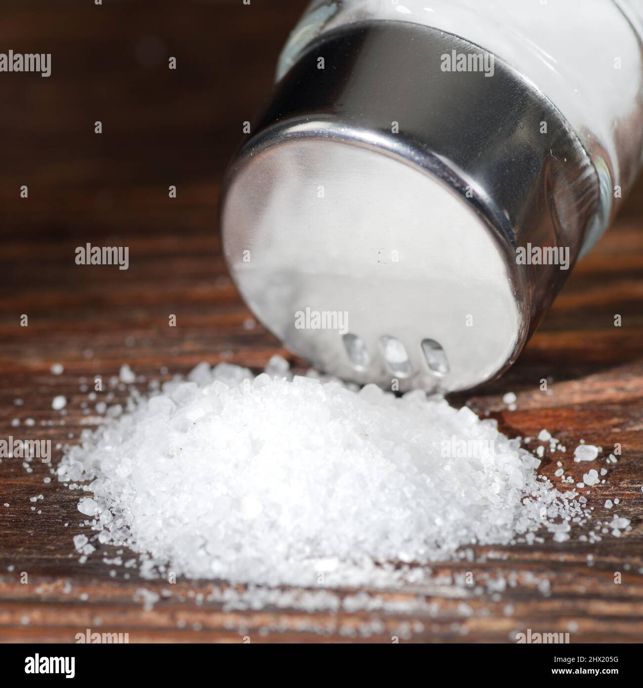 Salz aus einem Salzstreuer auf Holzgrund. Das Konzept der übermäßigen Salzaufnahme, die Ursache von Diabetes oder anderen Krankheiten sein kann Stockfoto
