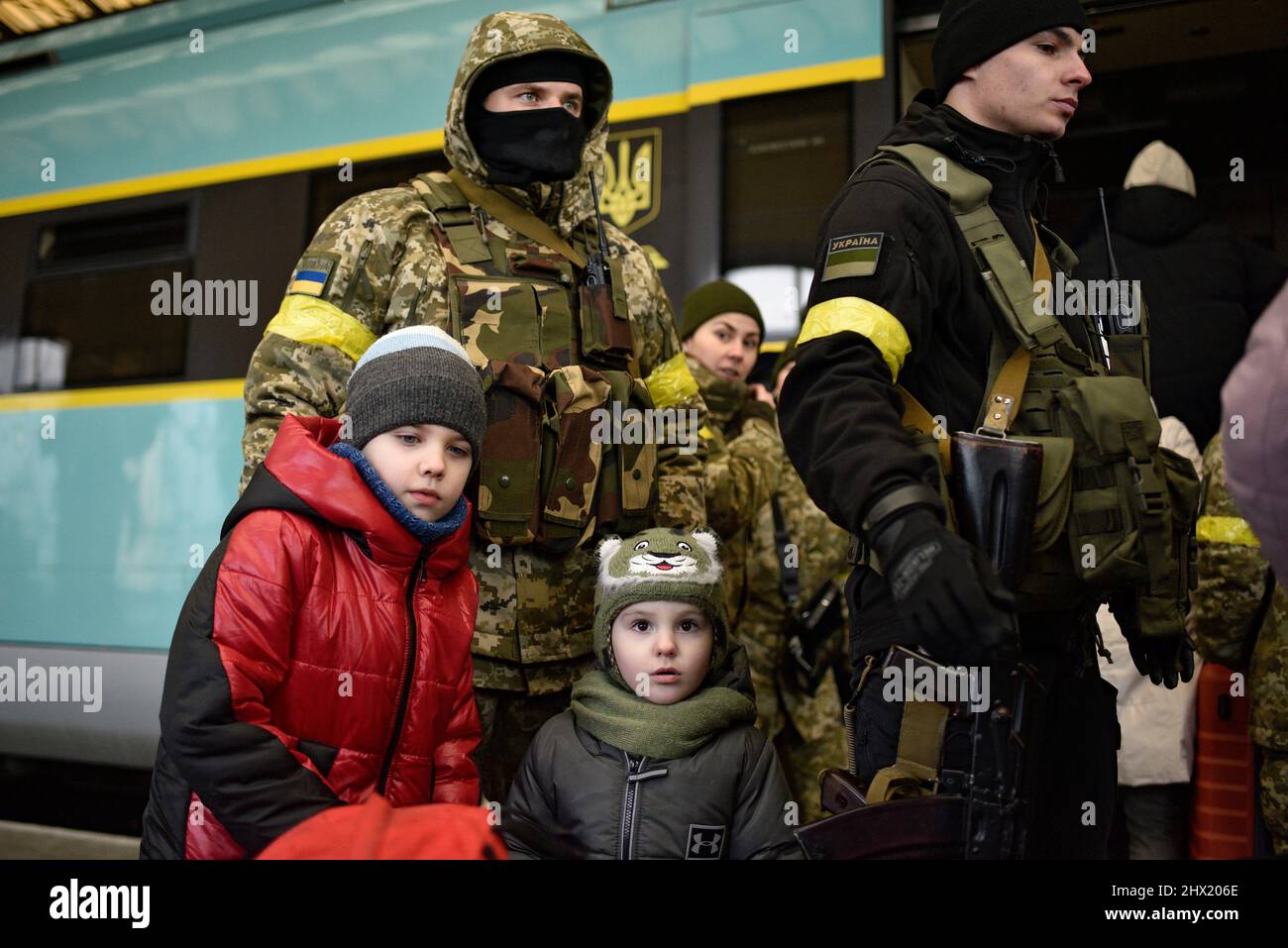 LVIV, UKRAINE - 28. FEBRUAR 2022 - zwei Kinder stehen vor Soldaten auf dem Bahnsteig am Bahnhof von Lviv, als Flüchtlinge, die vor Feindseligkeiten fliehen Stockfoto