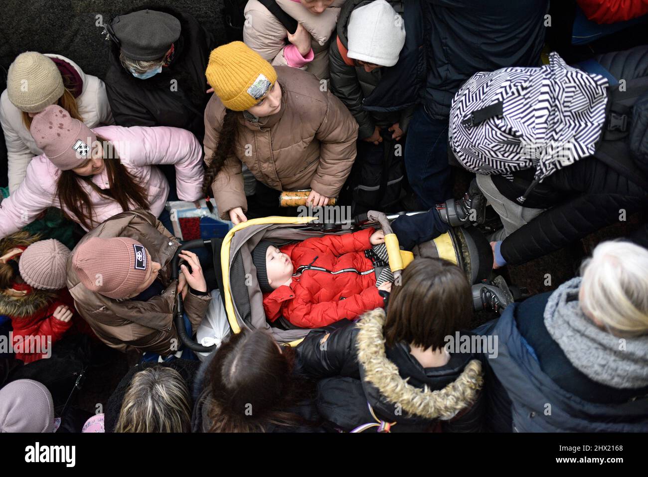 LVIV, UKRAINE - 28. FEBRUAR 2022 - Ein Baby schläft in einem Kinderwagen, der von Menschen am Bahnhof von Lviv umgeben ist, als Flüchtlinge vor den Feindseligkeiten an Bord von eva fliehen Stockfoto