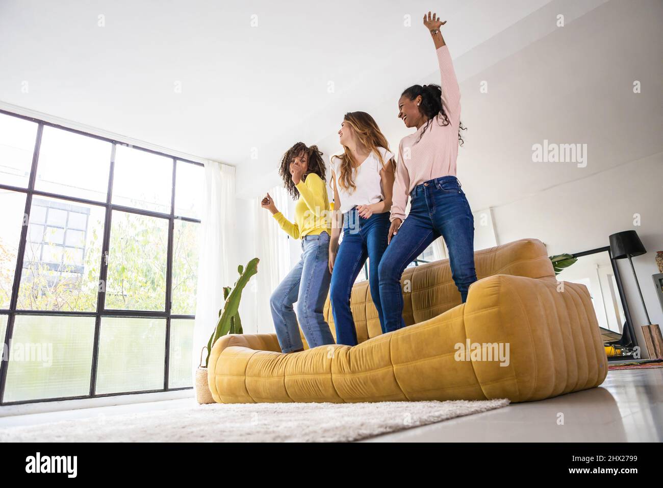 Drei junge Erwachsene Freundinnen, die Spaß haben, gemeinsam auf dem Sofa zu Hause zu tanzen Stockfoto