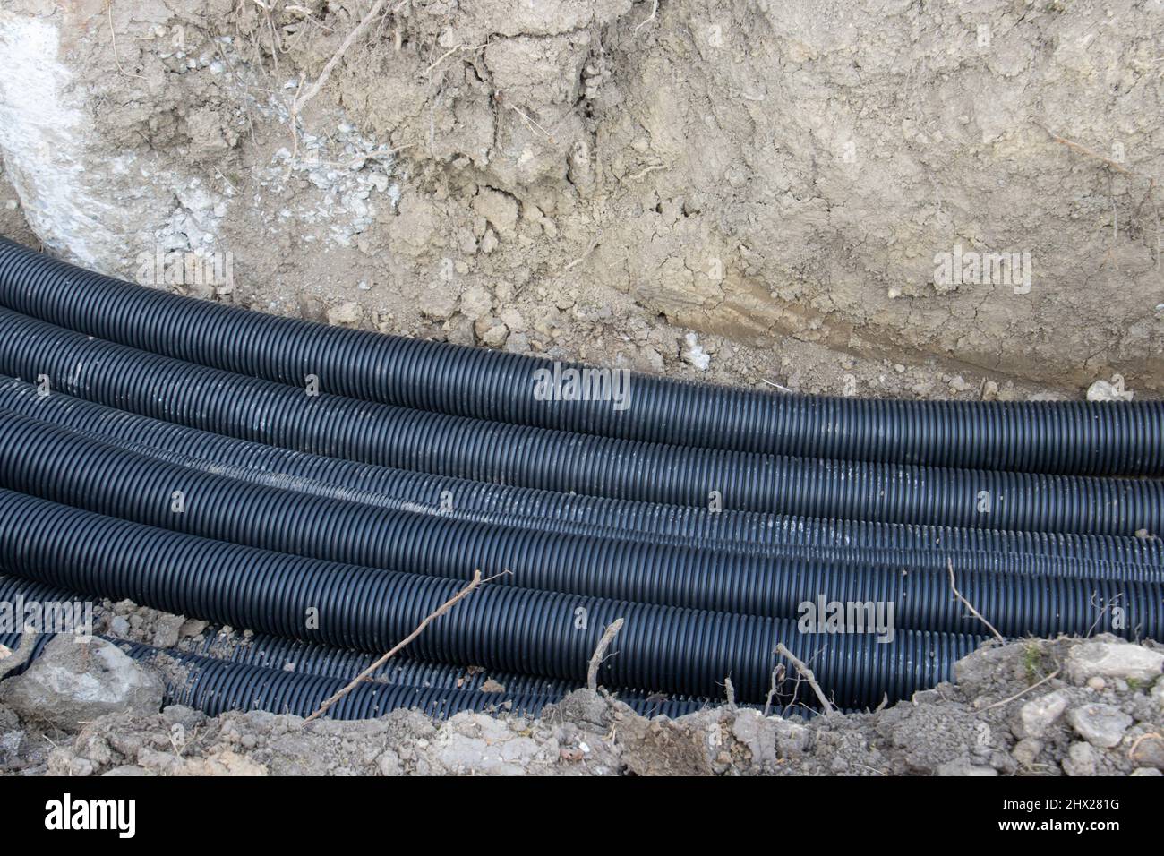 Schwarze Drainagerohre aus Wellkunststoff, die in einem Graben auf einer Baustelle verlegt werden Stockfoto