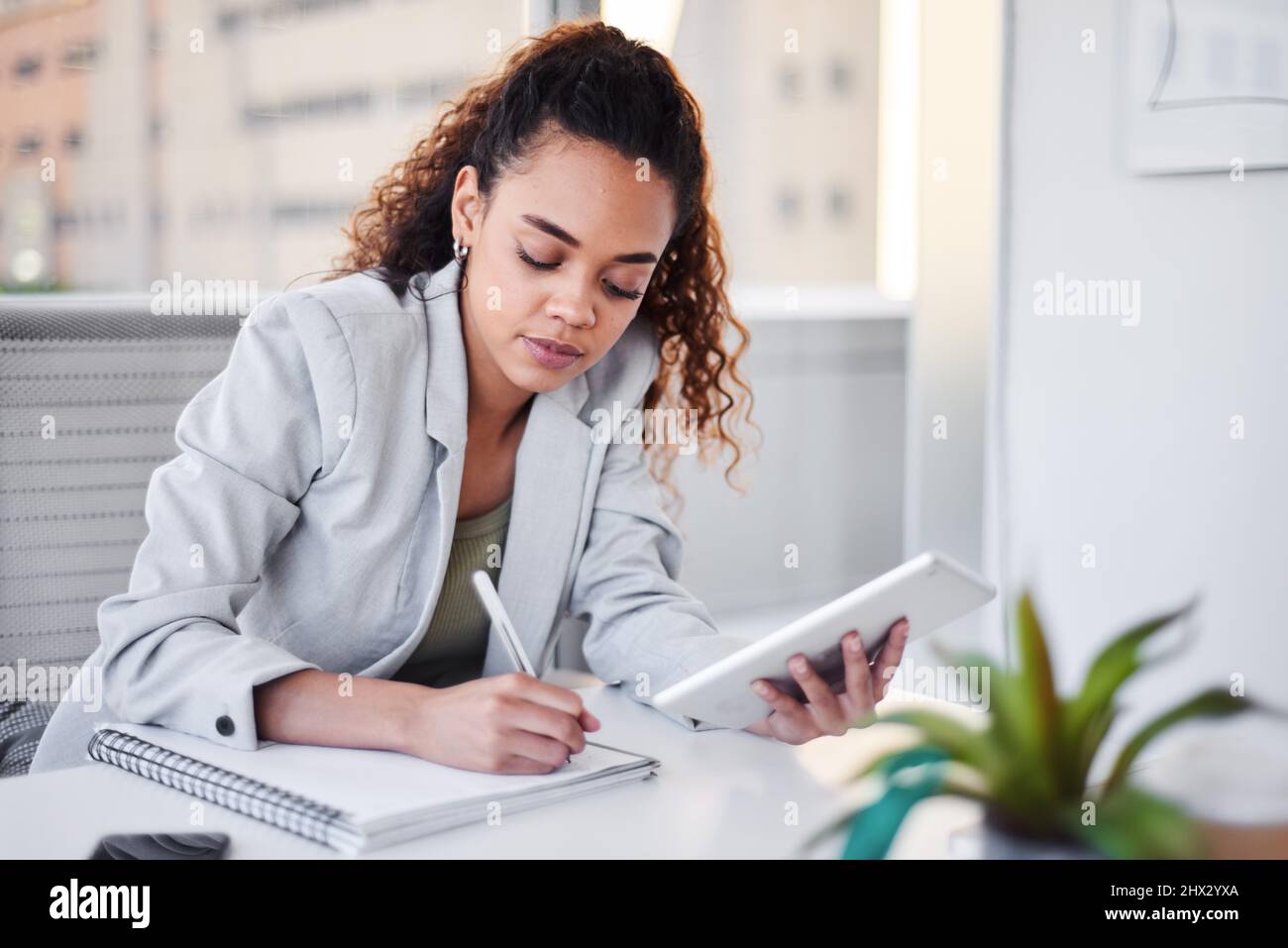 Eine junge Geschäftsfrau schreibt Notizen von ihrem digitalen Tablet in ein Notizbuch Stockfoto