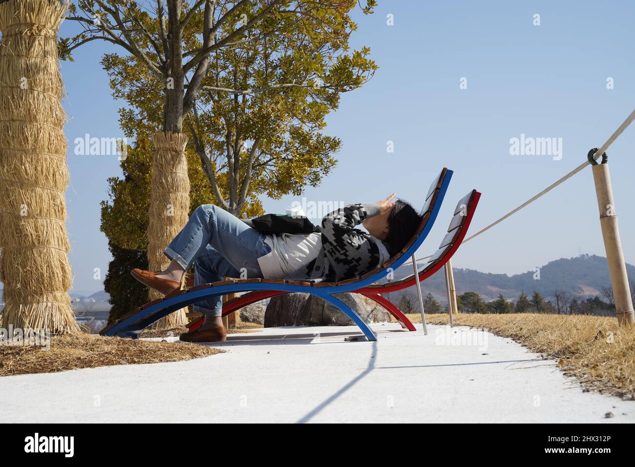 Es ist eine Bank unter ein paar Bäumen platziert, aber es ist schwer, die Augen zu öffnen, weil die Sonne auf Ihrem Gesicht scheint. Stockfoto