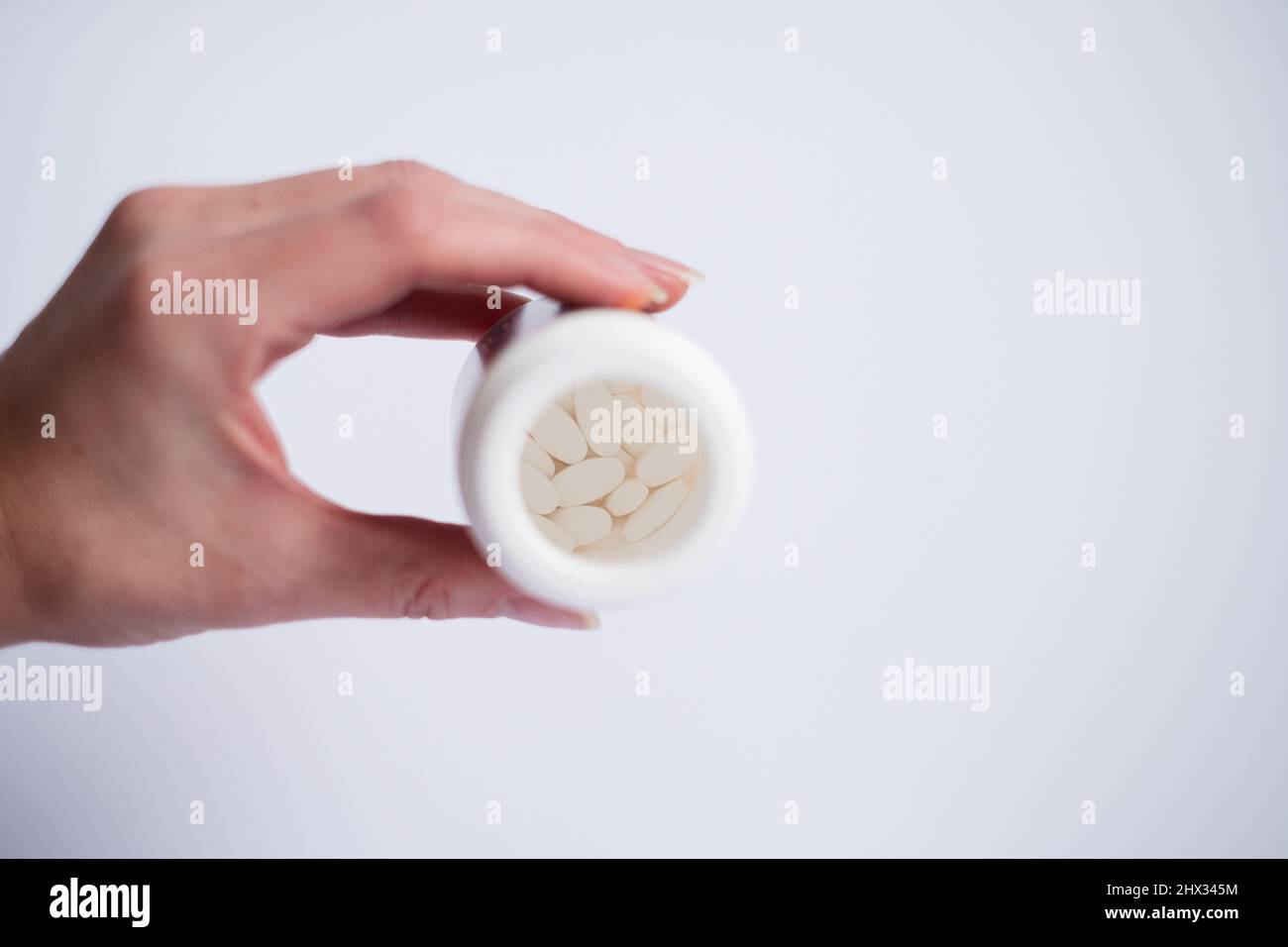 Weibliche Hand mit einer Flasche weißer Tabletten auf hellem Hintergrund. Selektiver Fokus in der Flasche auf Pillen. Stockfoto