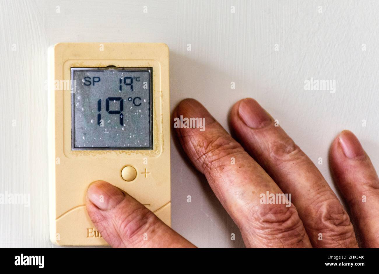Ein älterer, älterer, alter Mann passt die Temperatur seines Heims über einen digitalen Thermostat an, wenn die Heizkosten steigen. Stockfoto