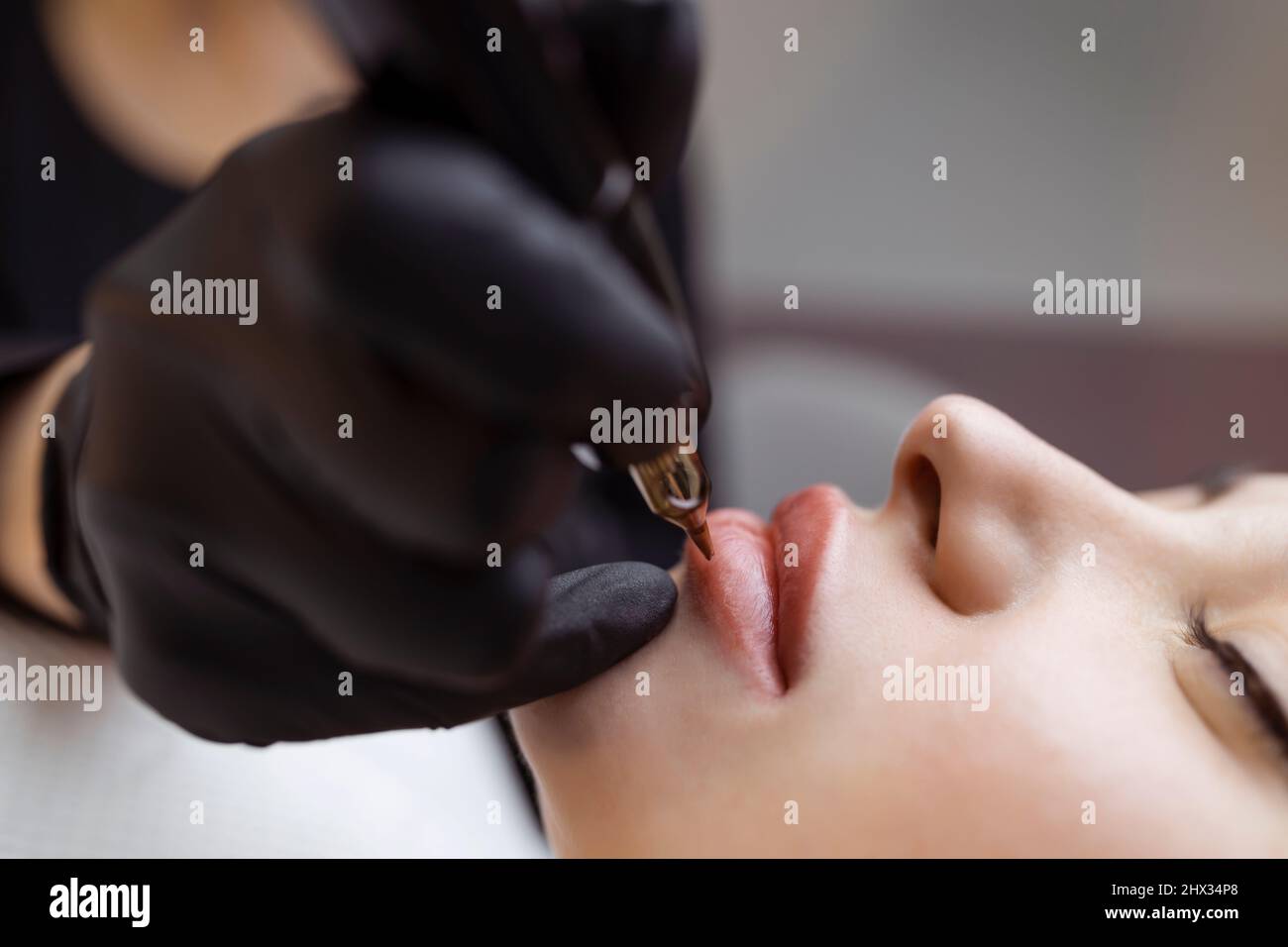 Der Kosmetologe macht dauerhaft Make-up auf dem Gesicht einer Frau. Spezialist trägt ein Tattoo auf die Lippen des Patienten Nahaufnahme Stockfoto