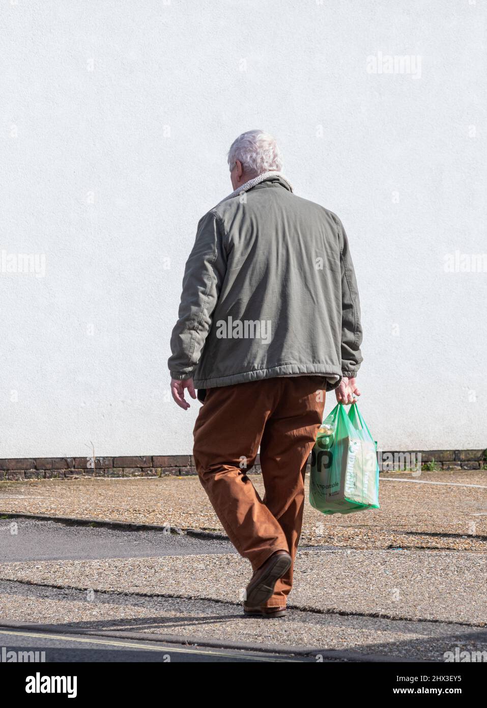 Älterer Mann, der aus dem Geschäft oder Geschäft zurückkommt und eine Co-op-Supermarkttasche aus Kunststoff trägt, Großbritannien Stockfoto