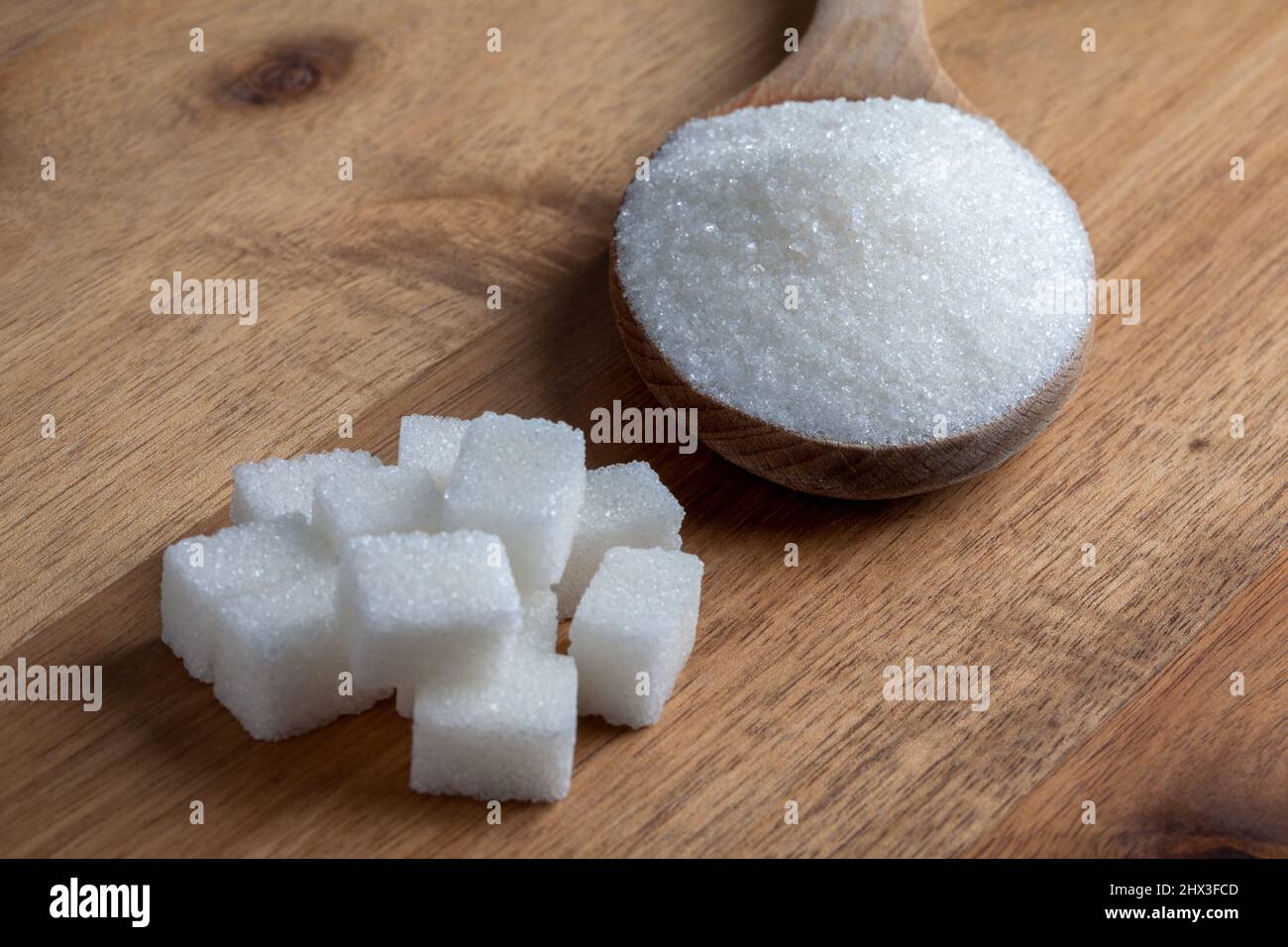Granulatzucker und Zuckerwürfel in Holzlöffel auf Holzboden Stockfoto
