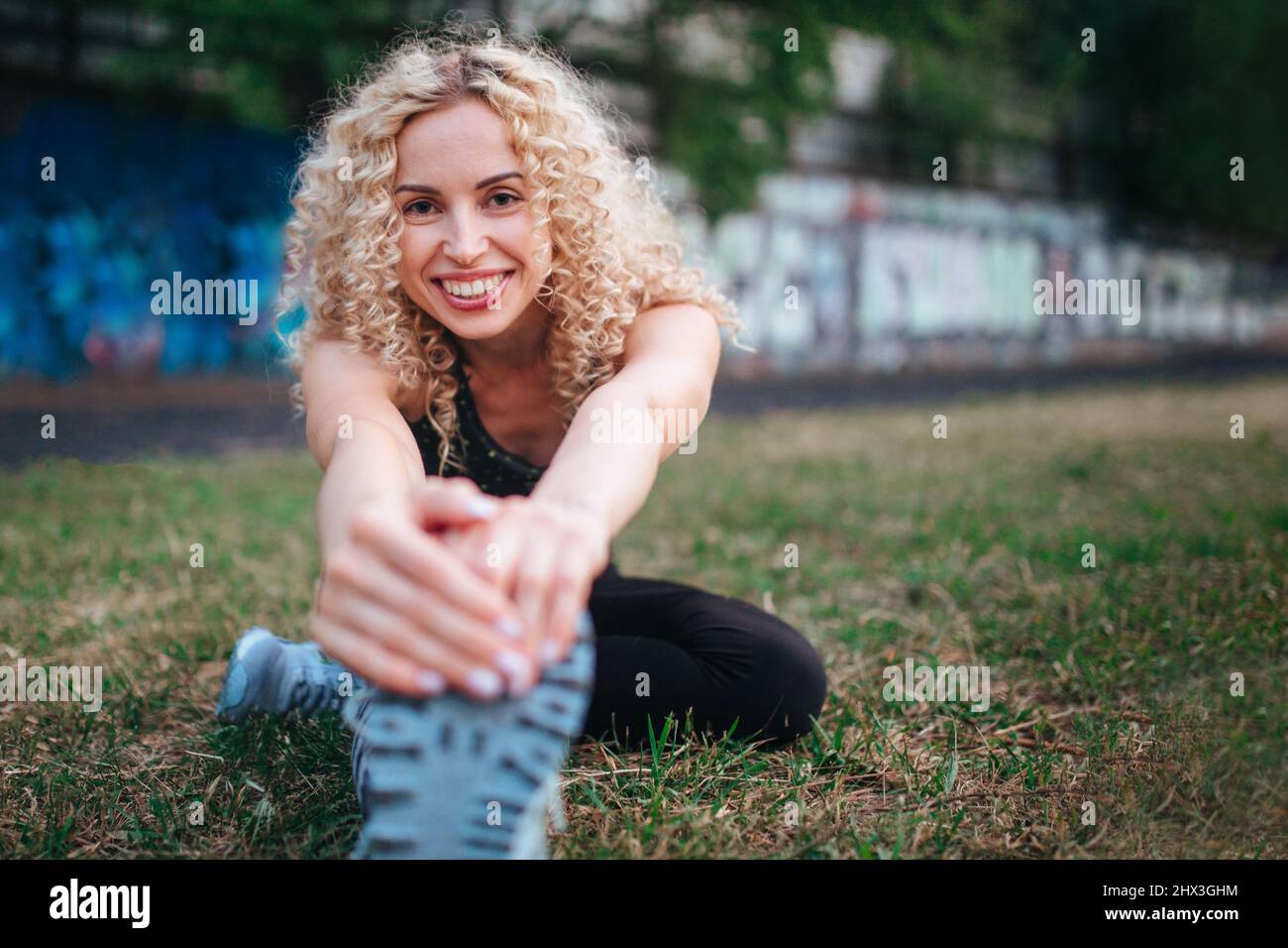 Eine junge, lockige Blondine mit athletischer Körperbau führt vor dem Training im Stadion ein Warm-up durch. Outdoor-Sport Stockfoto