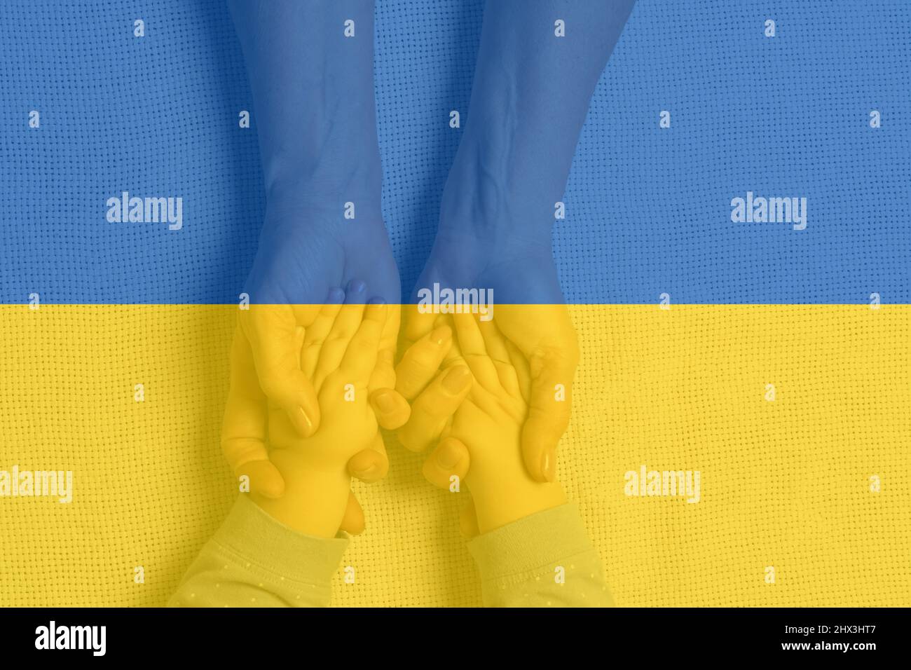 Menschliche Hände von Erwachsenen halten die Hände des Babys vor dem Hintergrund der ukrainischen Flagge. Das Konzept der Unterstützung und Unterstützung der Ukraine. Stockfoto