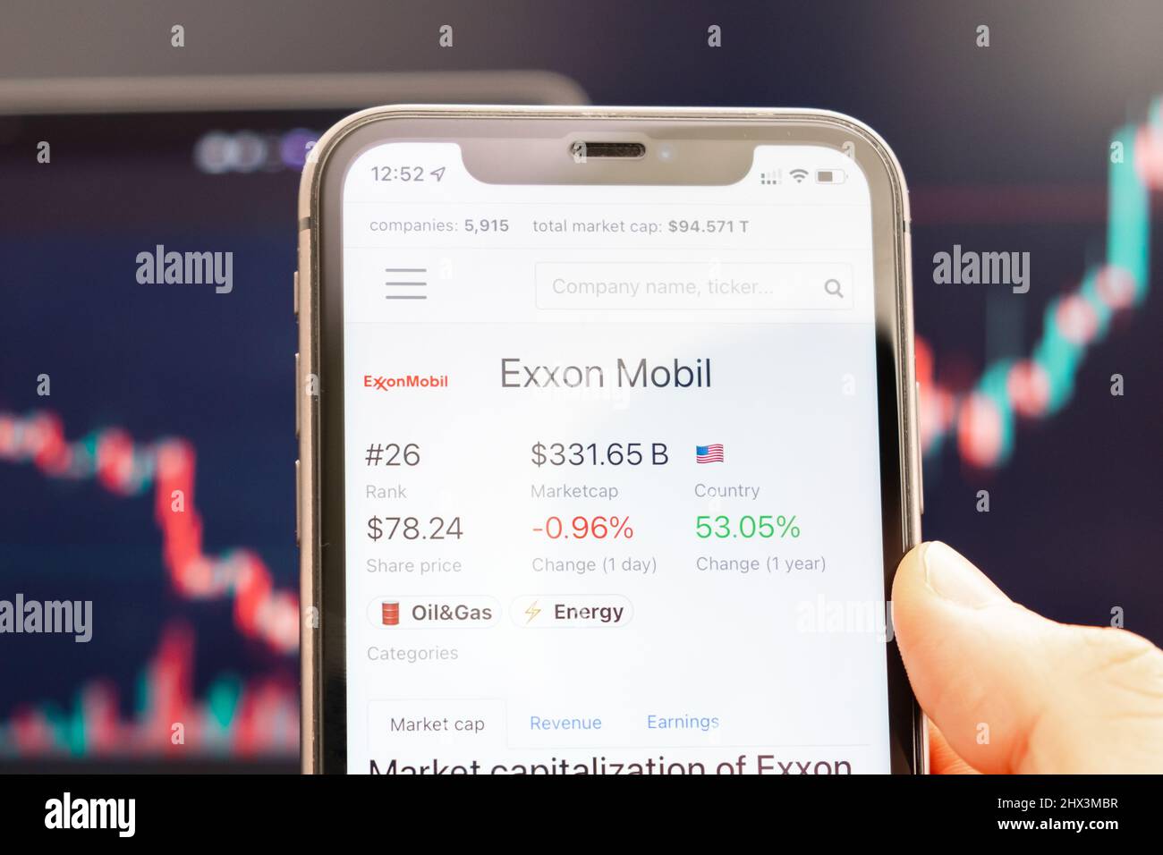 Exxon Mobil Aktienkurs auf dem Bildschirm des Mobiltelefons in mans Hand mit wechselnden Börsengraphen im Hintergrund, Februar 2022, San Francisco, USA. Stockfoto