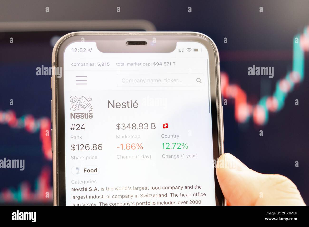 Nestle-Aktienkurs auf dem Bildschirm des Mobiltelefons in mans Hand mit wechselnden Börsengraphen im Hintergrund, Februar 2022, San Francisco, USA. Stockfoto