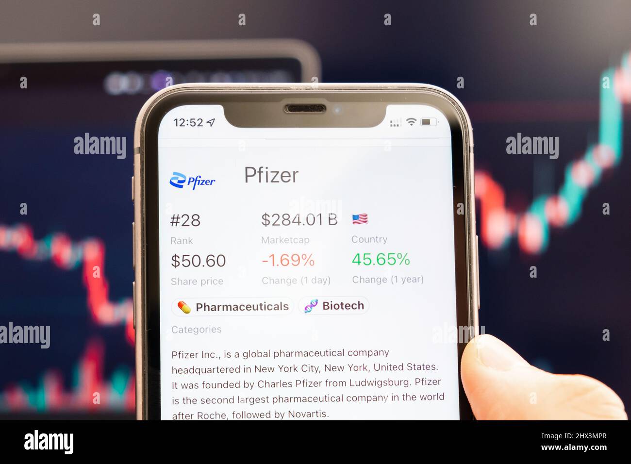 Pfizer-Aktienkurs auf dem Bildschirm des Mobiltelefons in mans Hand mit wechselnden Börsengraphen im Hintergrund, Februar 2022, San Francisco, USA. Stockfoto