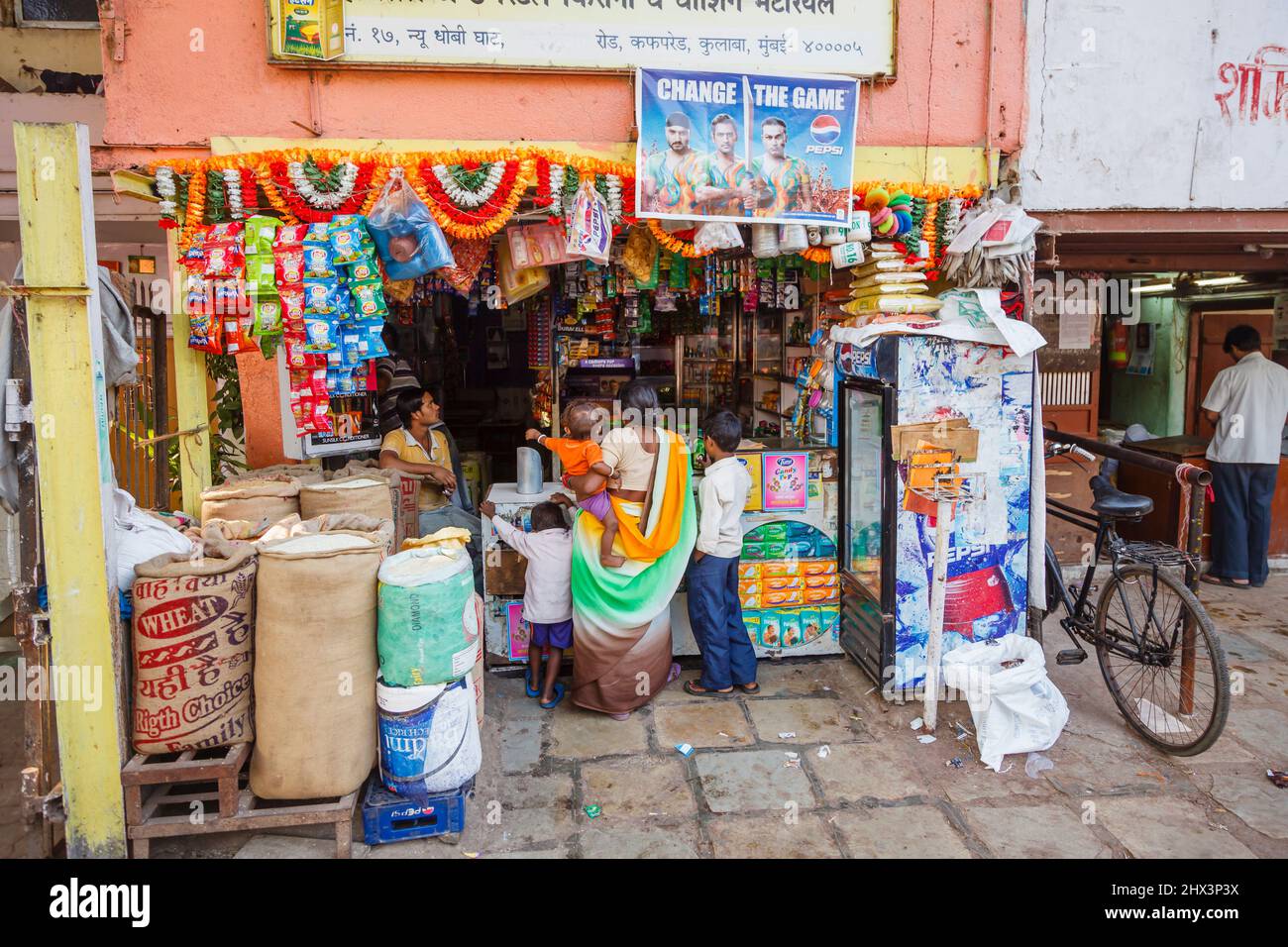 Eine einheimische Frau in einem Sari mit kleinen Kindern, eine Kundin in einem Lebensmittelgeschäft außerhalb von Mahalaxmi Dhobi Ghat, einer großen Open-Air-Wäscherei in Mumbai, Indien Stockfoto