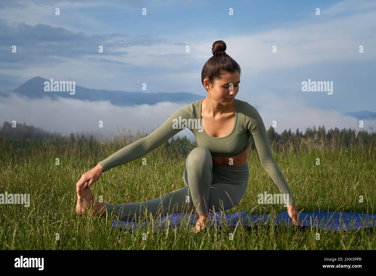Attraktive Frau mit dunklem Haar, die morgens in der Natur Yoga praktiziert. Junge weibliche Person in Sportkleidung Training regelmäßig für einen gesunden und gesunden Körper. Stockfoto