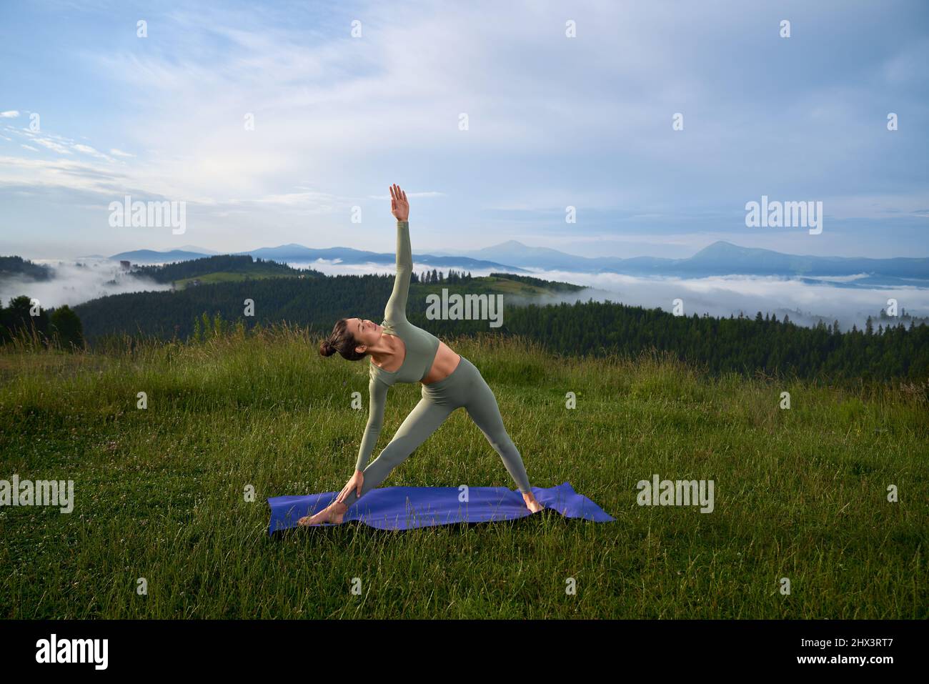 Schöne junge Brünette in Sportkleidung Yoga-Übung mit herrlichem Blick auf die Berge im Hintergrund zu üben. Aktives und gesundes Lebensstile-Konzept. Stockfoto