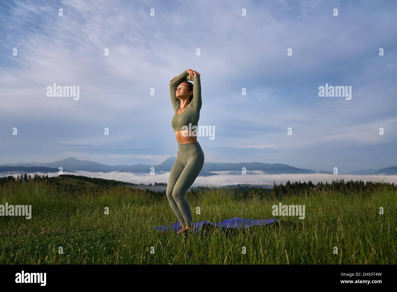 Attraktive Frau in Sportkleidung, die Yoga-Übungen in grünen Bergen macht. Konzentrations- und Harmoniekonzept. Stockfoto