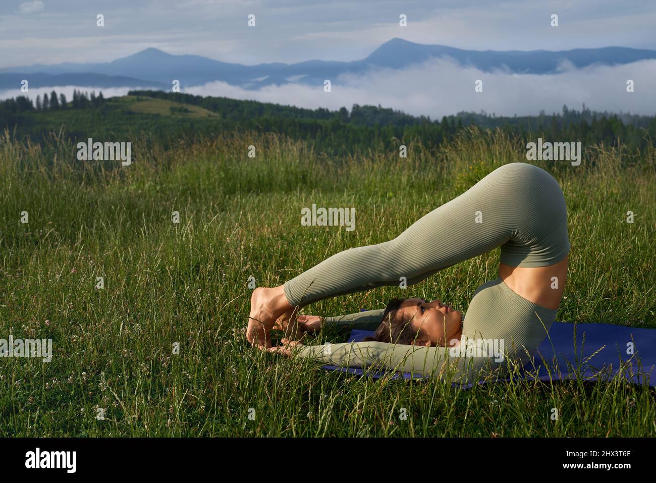 Flexible junge Frau mit dunklem Haar mit körperlicher Aktivität an der frischen Luft. Schlanke weibliche Person in Sportkleidung genießen Training mit Bergen auf dem Hintergrund. Stockfoto