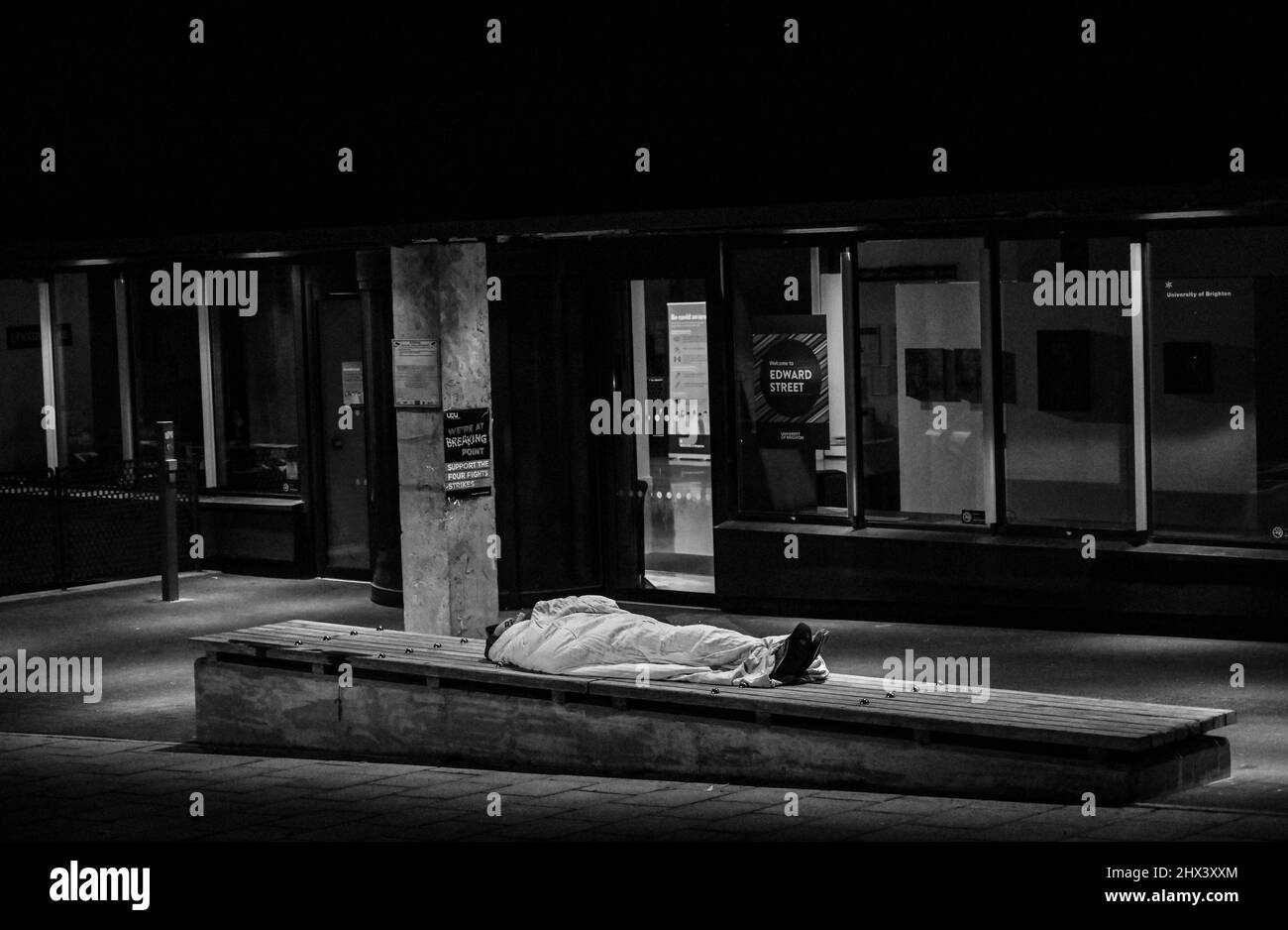 Mann, der auf einer Bank vor einem Eingang zu einem Gebäude der Universität von Brighton in der Edward Street schläft Stockfoto