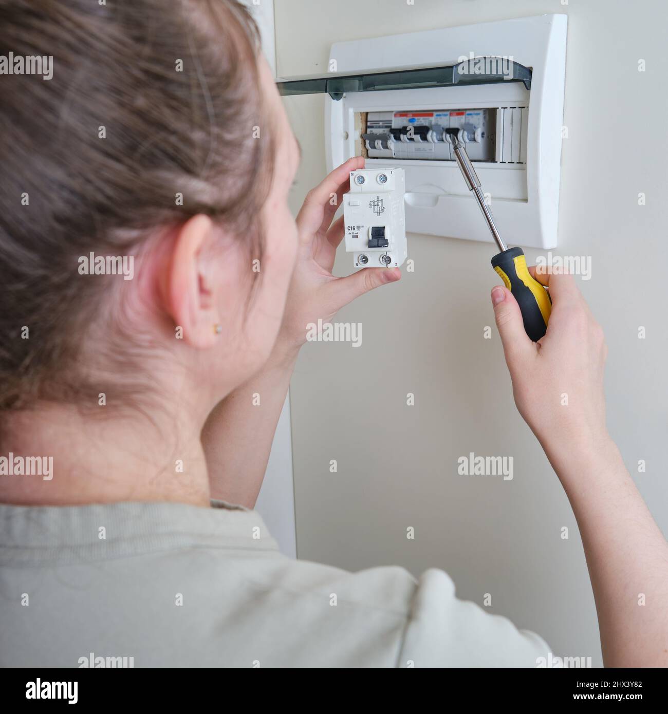 Eine Frau wechselt eine automatische Sicherung in einer Hauselektrik. Selbstreparatur und Austausch von elektrischen Geräten in der Wohnung, diy Stockfoto