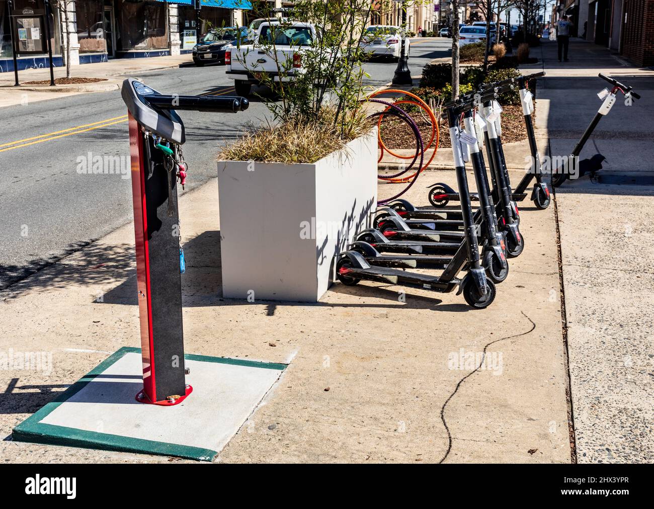 GASTONIA, NC, USA-3. MÄRZ 2022: Kostenloses Fahrrad-Service-Center (Stange) und Vermietung von Motorroller auf dem Bürgersteig aufgereiht. Stockfoto