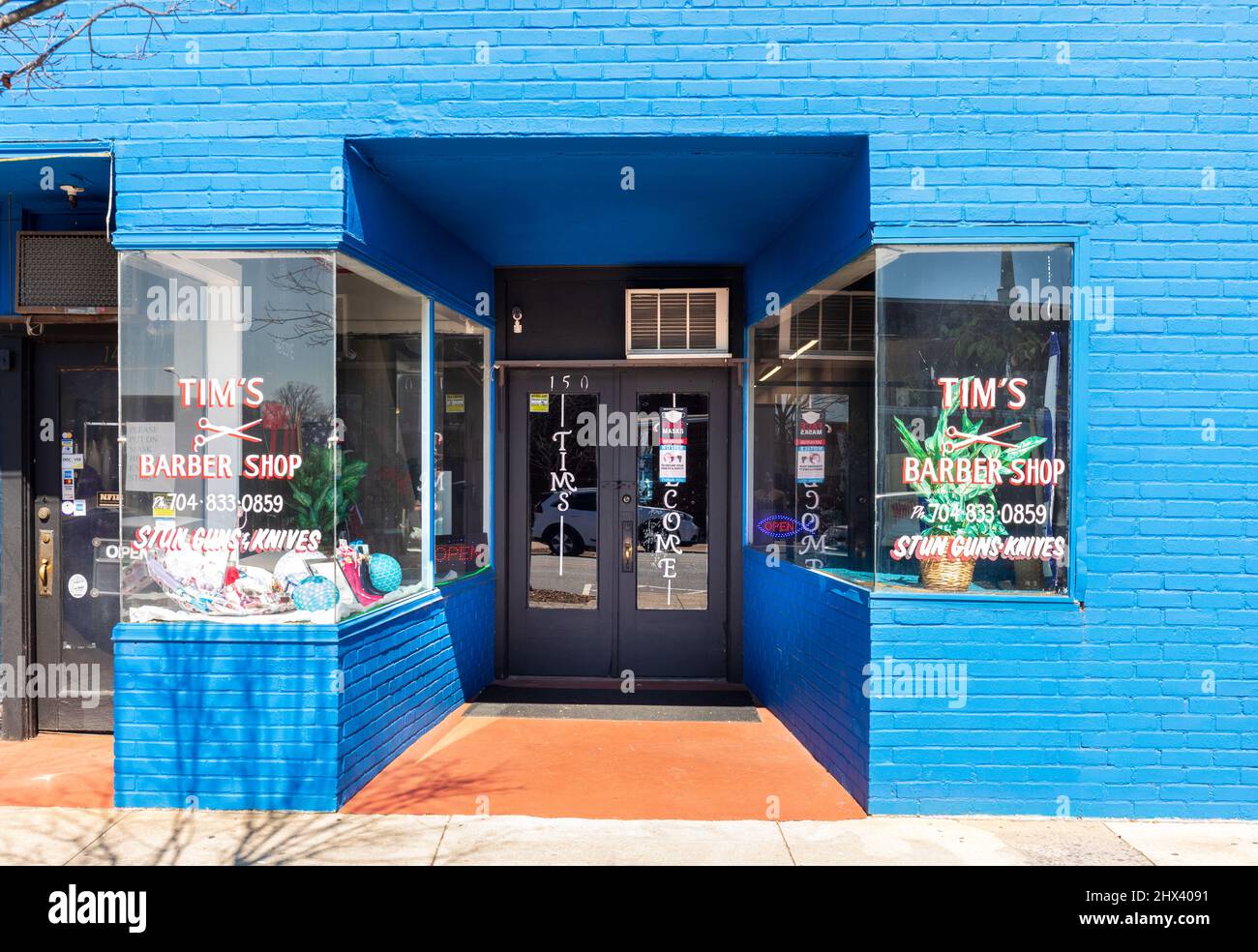 GASTONIA, NC, USA-3 MARCH 2022: Tim's Barber Shop, Eingang und Schaufenster für Elektroschocker und Messer. Stockfoto