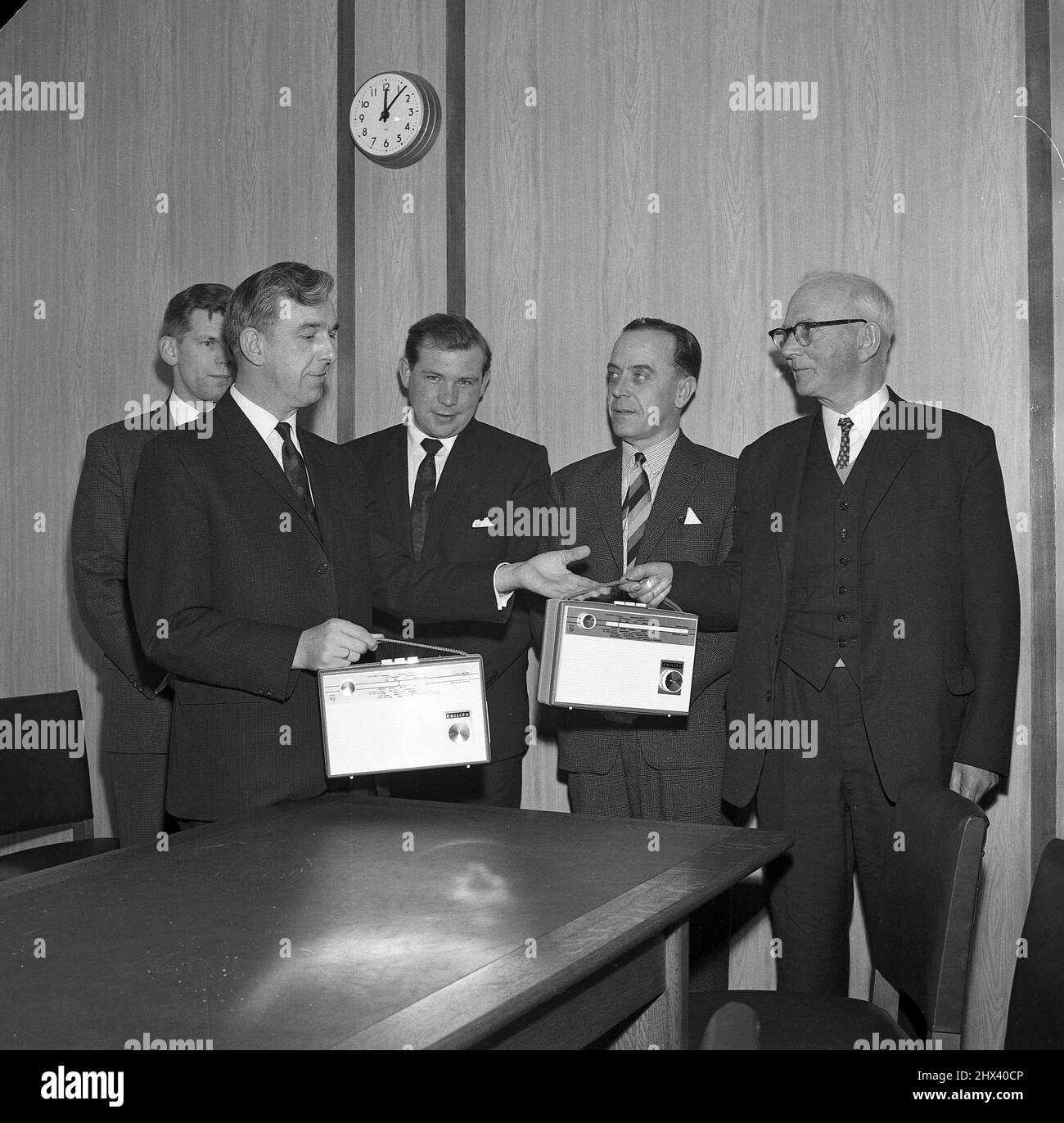 1960s, historisch, stehend im Vorstandszimmer des Unternehmens, eine Reihe von geeigneten Unternehmensleitern, zwei mit ihren Produkten, tragbare Transistor-Radios, England, Großbritannien. Stockfoto