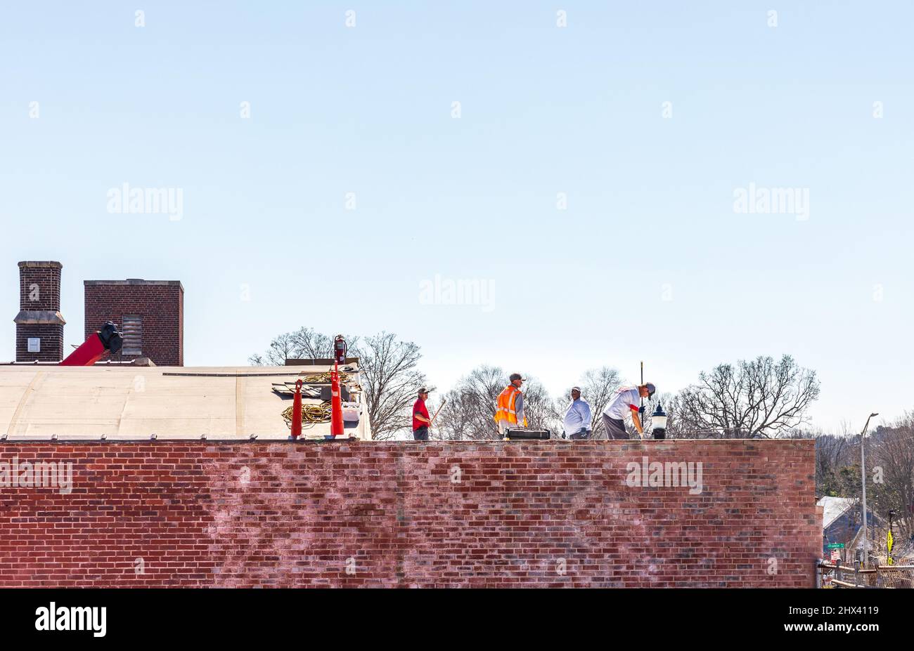 GASTONIA, NC, USA-3 MARCH 2022: Vier Arbeiter auf einem Flachdach-Geschäftsgebäude. Bau, Dach, Arbeiter. Stockfoto