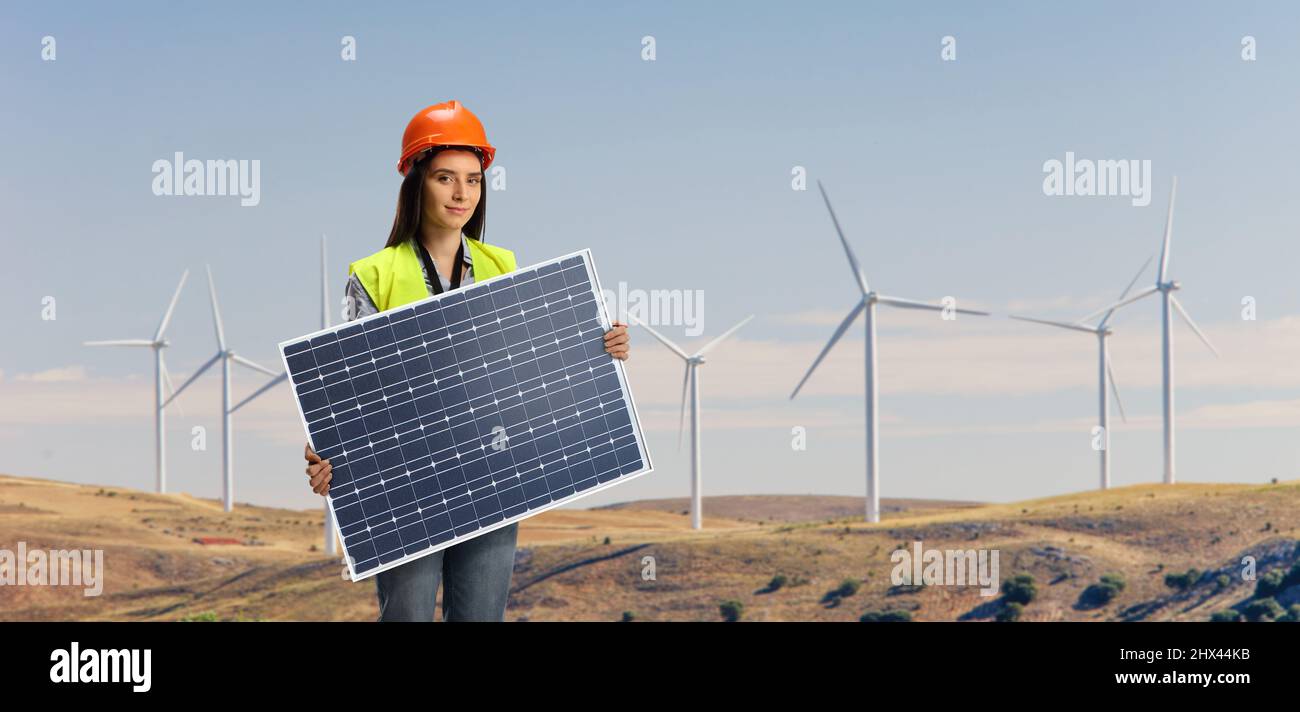 Eine Ingenieurin, die ein Photovoltaik-Solarpanel auf einem Windturbinenfeld hält Stockfoto