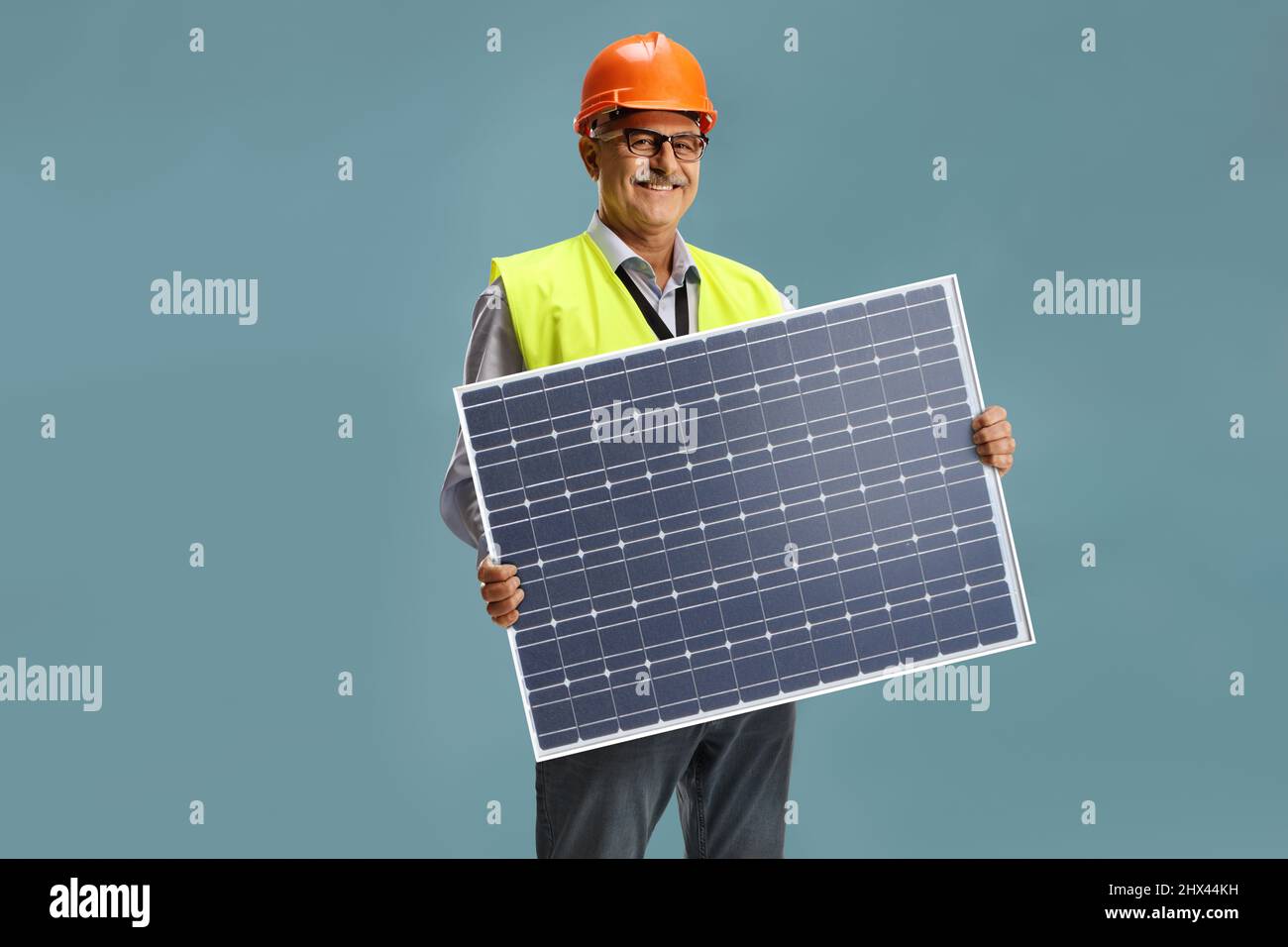 Lächelnder männlicher Ingenieur, der eine Photovoltaikanlage auf blauem Hintergrund isoliert hält Stockfoto