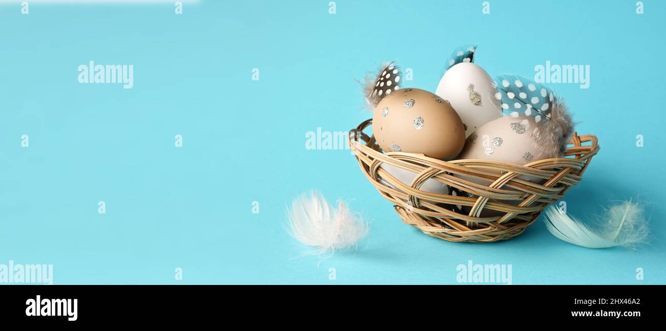 Ostereier in einem Nest mit Federn auf blauem Hintergrund. Urlaubskonzept. Stockfoto