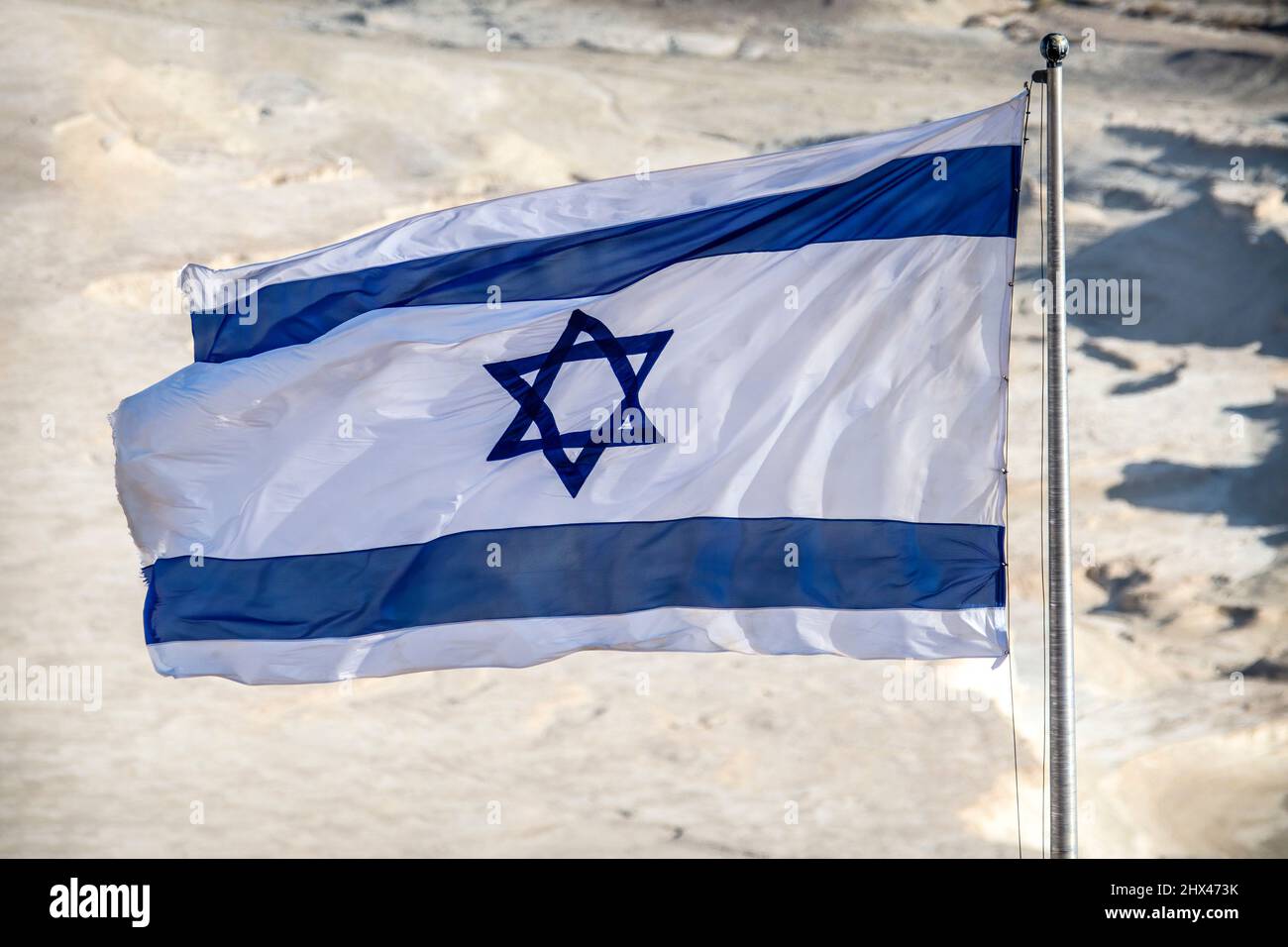 Die israelische Flagge fliegt bei Sonnenschein über der Wüstenkulisse Stockfoto