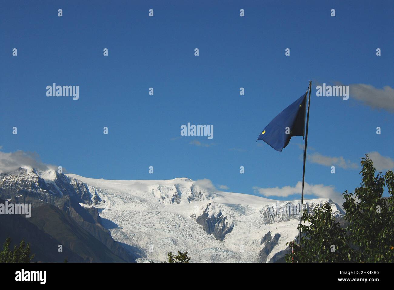 Die zerfetzte Alaska-Staatsflagge, die im Vordergrund eines Panoramas auf den schmelzenden Kennicott-Gletscher im Alaskan Wrangell St. Elias nationa fliegt Stockfoto