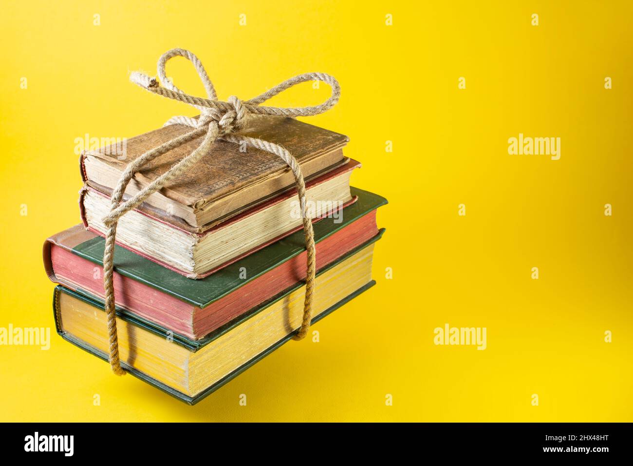 Vintage-Bücher wurden mit einem Jutesteil auf gelbem Hintergrund abgesteckt und gebunden Stockfoto