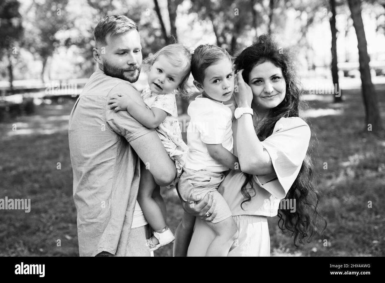 Fürsorgliche Eltern mit kleinen Kindern im Park, schöne Mutter halten in den Armen freudigen Sohn, nette Tochter sitzt in Papa Hände, Familie verbringen Zeit zusammen, enj Stockfoto