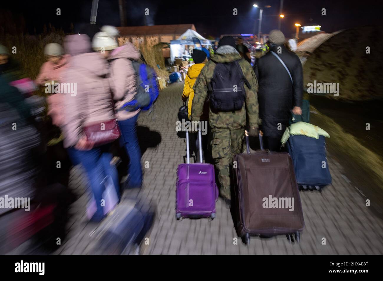 Medyka, Polen. 09. März 2022. Ein Mann in Tarnkleidung hilft Flüchtlingen aus der Ukraine, ihre Koffer am Grenzübergang zu ziehen. Am 24. Februar drangen russische Truppen in die Ukraine ein. Quelle: Sebastian Gollnow/dpa/Alamy Live News Stockfoto