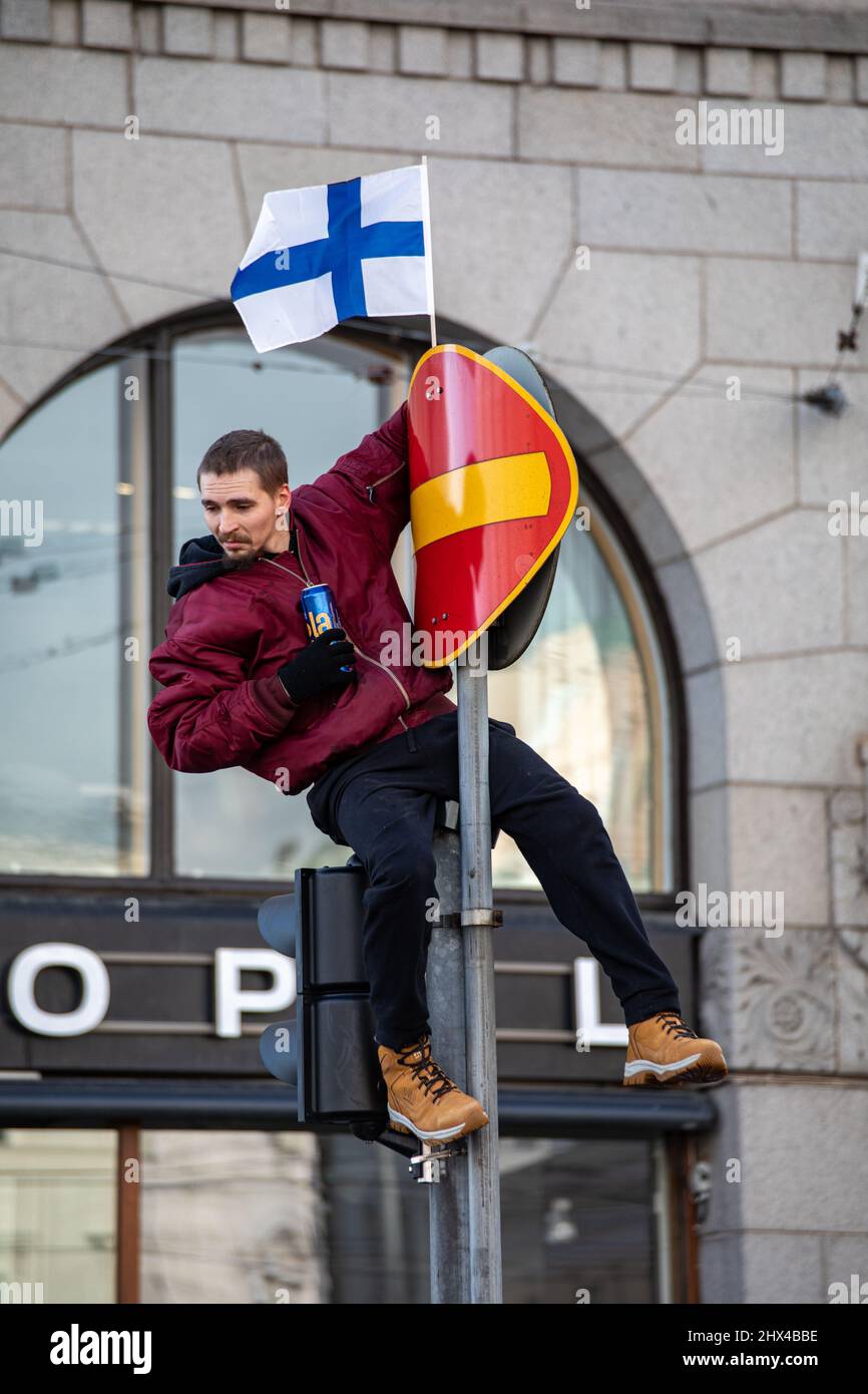 Junger Mann mit einer Miniatur-Flagge Finnlands und einer Dose Bier klettert auf einem Verkehrsschild in Helsinki, Finnland Stockfoto