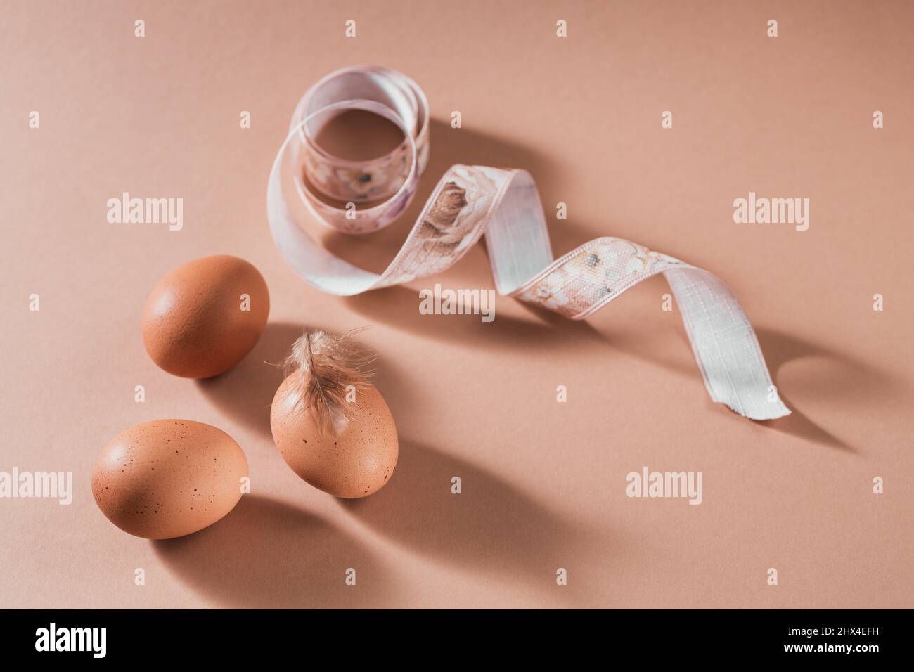 Frohe Osterkarte mit Eiern in natürlicher Farbe und Federn auf beigem Hintergrund Stockfoto