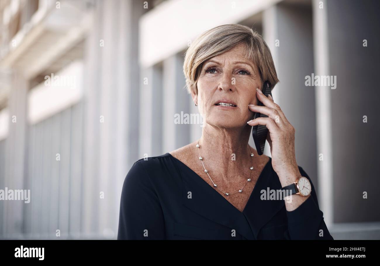 Nehmen Sie diesen Anruf an und handeln Sie. Aufnahme einer reifen Geschäftsfrau, die ein Smartphone vor einem Stadthintergrund benutzt. Stockfoto