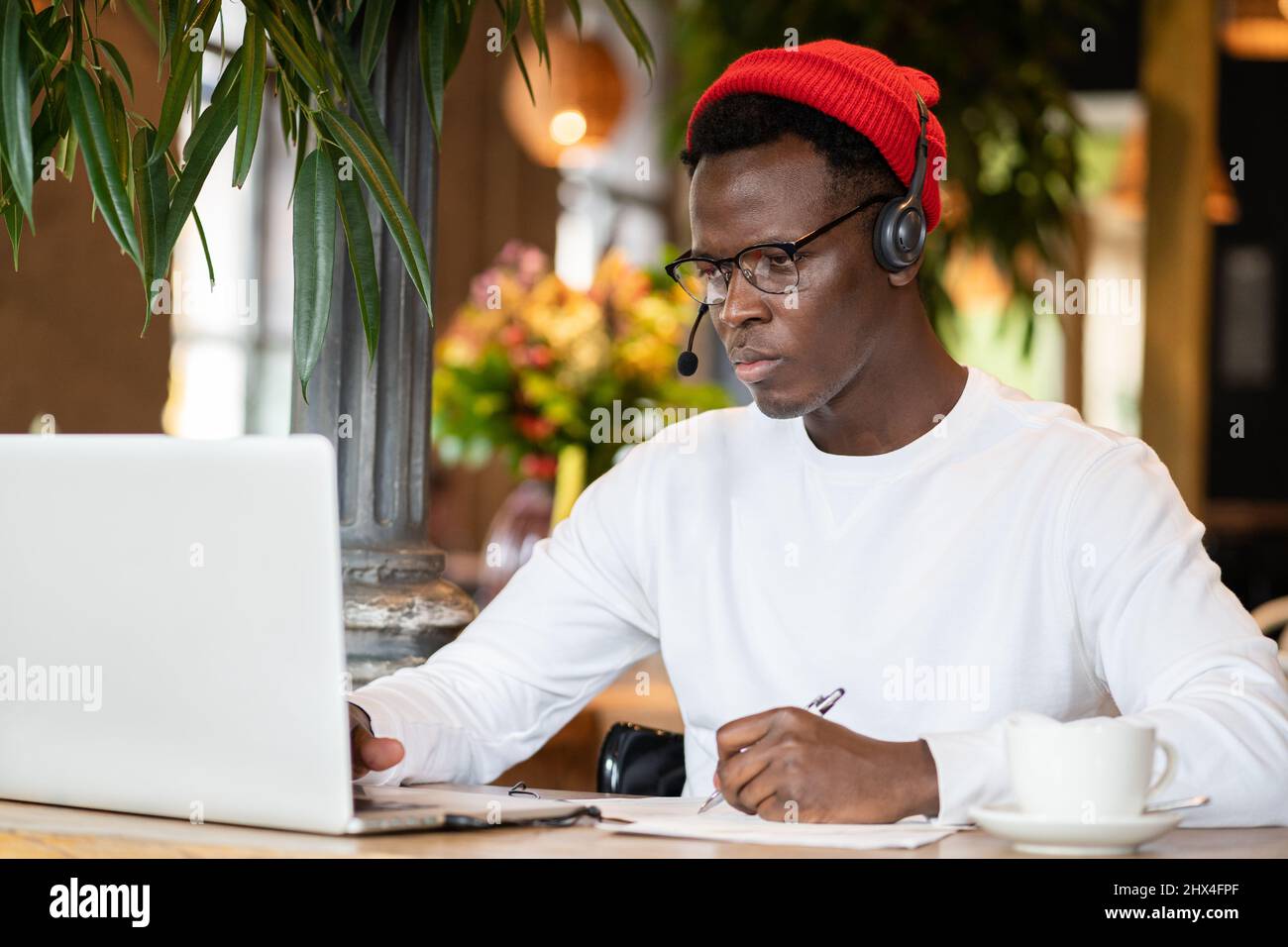 Konzentration schwarzer Hipster männlich in Kopfhörern, Brillen Studing oder Remote am Computer arbeiten Stockfoto