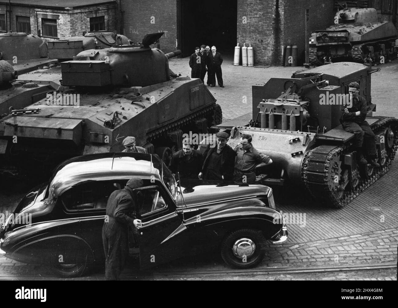 Dieses neue britische Auto wurde in eine Fabrik in Elswick, Newcastle-on-Tyne, geschickt, damit die Arbeiter die Art von Exportmodellen sehen konnten, zu deren Herstellung sie beigetragen haben. Eine in ihrem Werk produzierte 120-Tonnen-Presse stanzt nun stromlinienförmige Karosserien für das Auto. Im Hintergrund ist ein Sherman-Panzer, der noch bewaffnet ist und in einen schweren Bulldozer verwandelt wird. 27. Juli 1948. (Photo by Mirror Features). Stockfoto