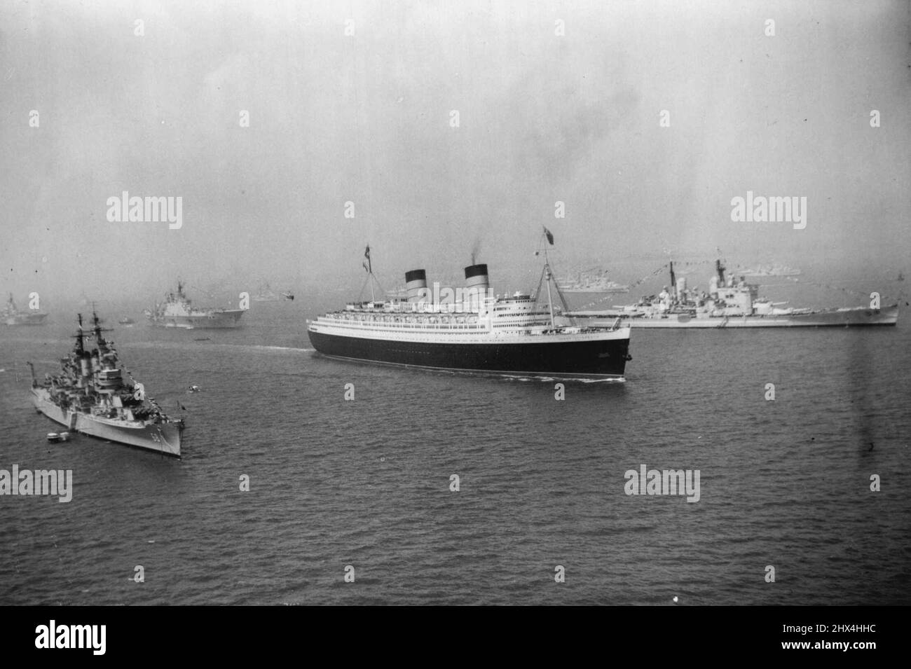 Queen Elizabeth Sails Through Review - das Luxusliner Queen Elizabeth segelt für die Vereinigten Staaten an einigen der Kriegsschiffe vorbei, die am 15.. Juni ihre Position bei Spithead für die Überprüfung der Flotte durch die Queen einnehmen. Auf der rechten Seite des Bildes ist das britische Schlachtschiff Vanguard, und auf der linken Seite ist der amerikanische Cruiser Baltimore. 11. Juni 1953. (Foto von Planet News Ltd.). Stockfoto