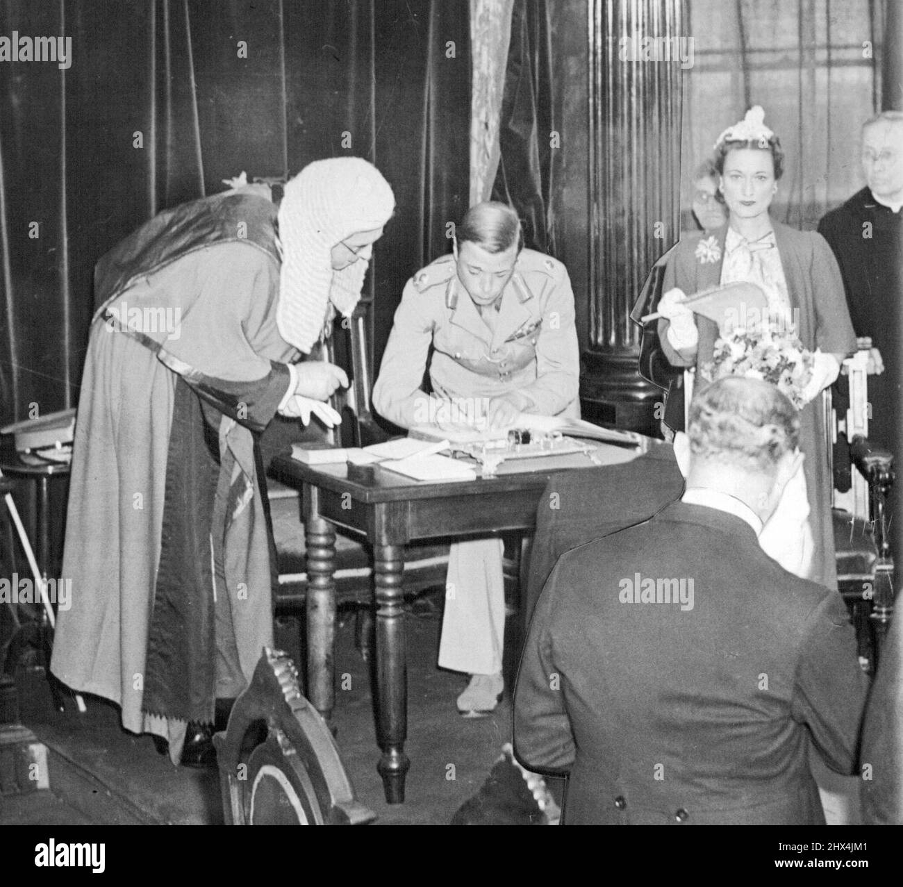 Eid an Bruder der Herzog von Windsor, ehemaliger Edward VIII. Von Großbritannien, unterzeichnet seinen Namen am 17. August, um einen Eid zu leisten, der seinem Bruder, König George VI., Treue verspricht, während er seine Pflichten in Nassau als Generalgouverneur der Bahamas übernimmt. Edward's in Amerika geborene Herzogin steht rechts, bewegt einen Fan und Chief Justice O.B. Daly, der die Roben seines Büros trägt, ist Zeuge der Unterschrift. 18. August 1940. (Foto von Associated Press Photo). Stockfoto
