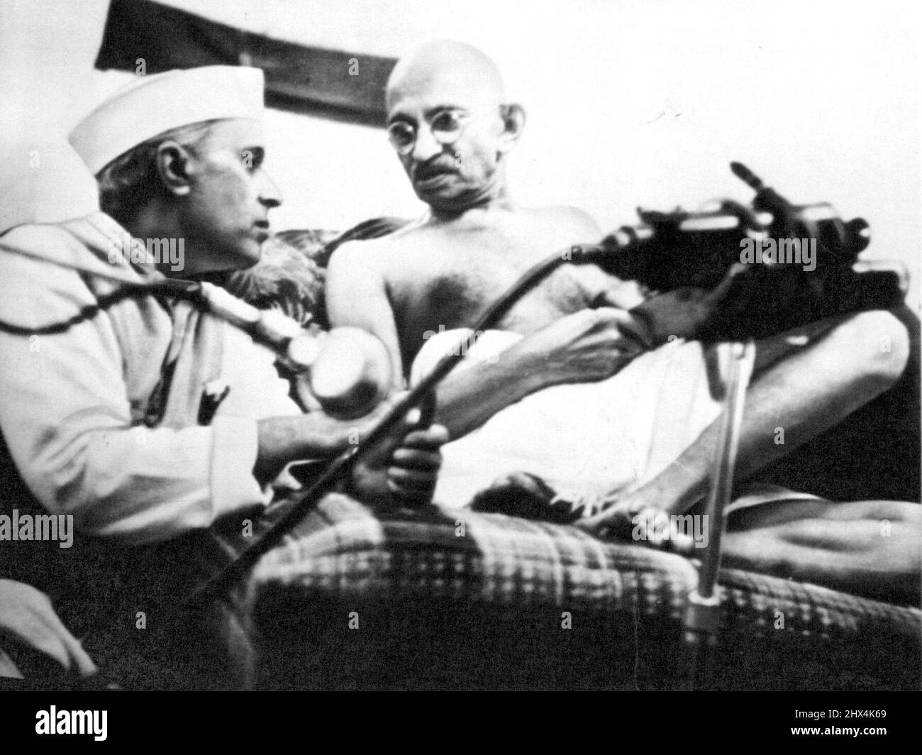 Polsterkonferenz -- Pandit Jawaharlal Nehru und Mohan das K. Gandhi, letztere bequem auf Kissen liegend, geben während der All-India Congress-Sitzung in Bombay einige Stunden vor ihrer Verhaftung am 8. August die Konferenz. Gandhi wurde heute 73 Jahre alt. Und 2.000 seiner Anhänger feisten seinen Geburtstag, indem sie Steine auf die Polizei warfen. 02. Oktober 1942. (Foto von AP Wirephoto). Stockfoto