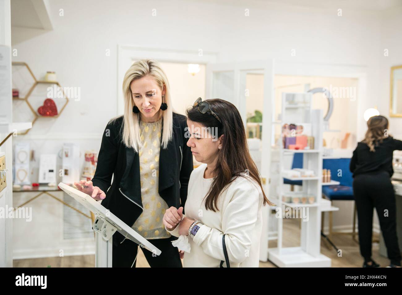 Eine Frau hilft einer anderen Frau, digital in ein Wellness-Spa für Schönheitsbehandlungen einzuchecken Stockfoto