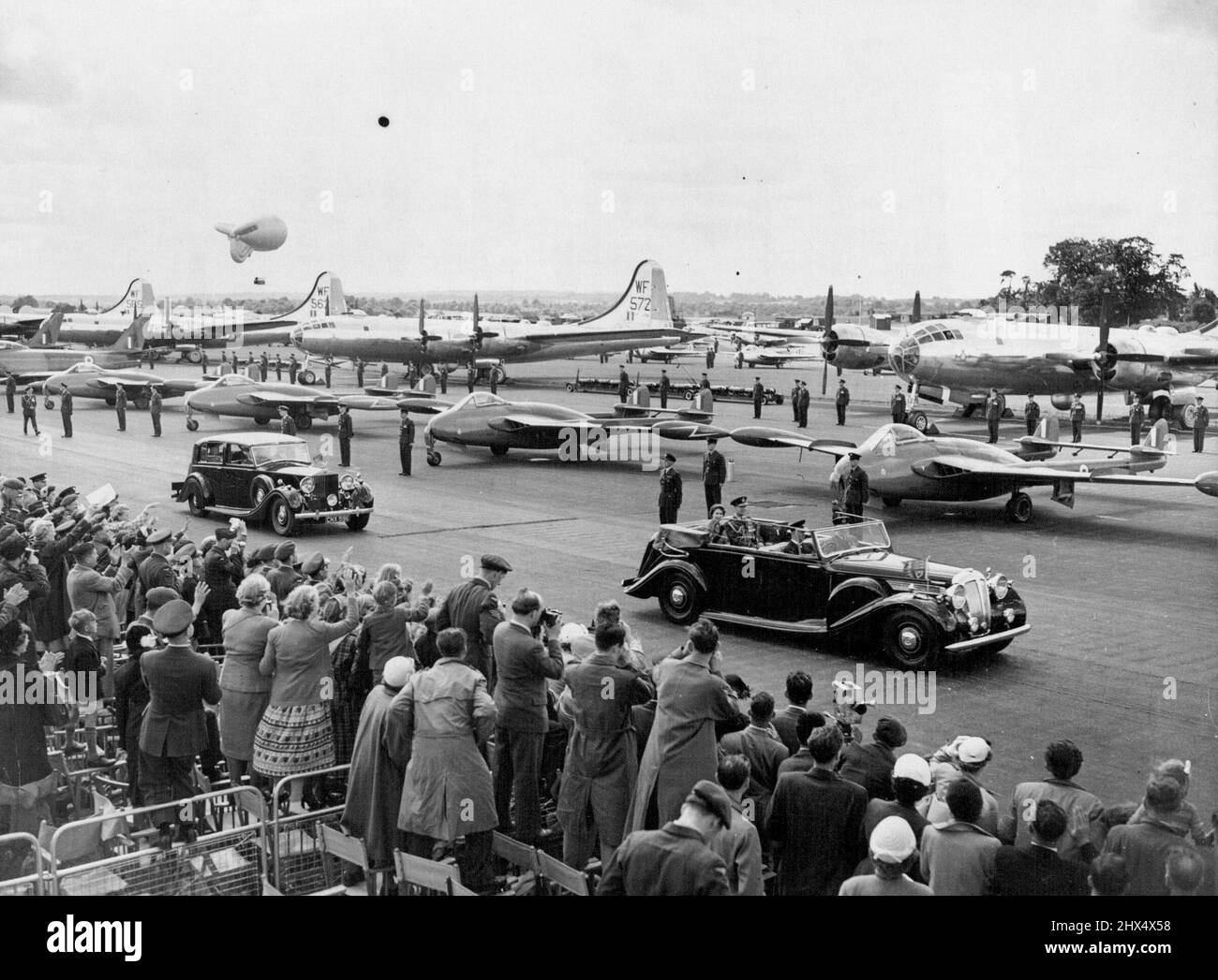 Queen and Duke Zwischen Jets und der Menge bei Coronation Air Review -- die Queen und der Duke of Edinburgh fahren in einem offenen Auto an einer Reihe von Venom-Düsenjägern bei der heutigen Überprüfung vorbei. Hinter den Kämpfern stehen schwere Bomber. Der Herzog ist in der Uniform des Marschalls der R.A.F. zu sehen Im Vordergrund sind Mitglieder der Menge beim Fotografieren des königlichen Paares zu sehen. Die Königin führte heute (Mittwoch) in Begleitung des Herzogs von Edinburgh ihre Krönungsüberprüfung der königlichen Luftwaffe am R.A. F. Bahnhof, Odiham, Hampshire, durch. Mit 318 Flugzeugen am Boden und über 600 an einem Vorbeiflug, die Wiederbelebung Stockfoto