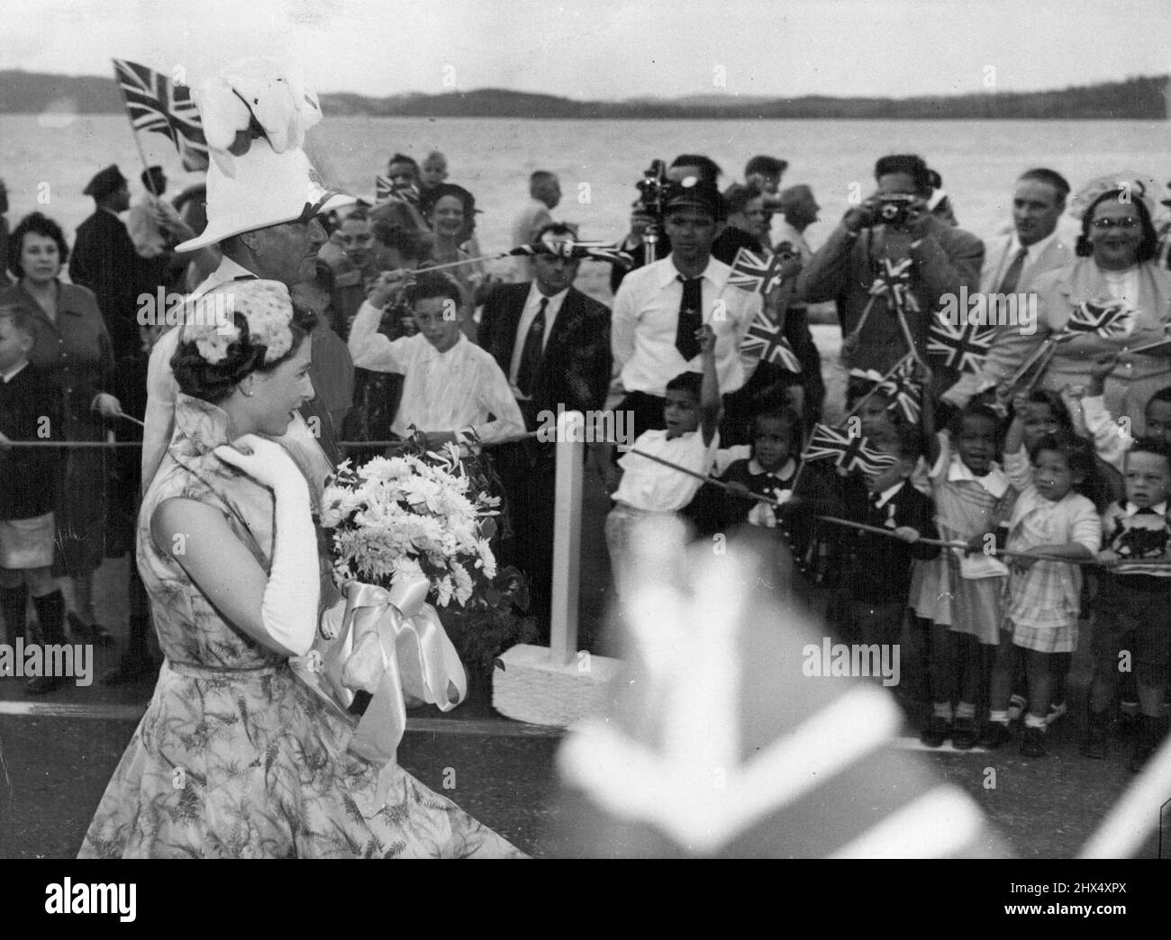 Die Königin auf Bermuda -- die Königin geht mit dem Gouverneur von Bermuda, LT. General Sir Alexander Hood, durch eine Gasse jubelender Kinder, kurz nachdem sie ihr Flugzeug bei der Ankunft in freundlicherweise Field, Bermuda, November 24, verlassen hat. Ihre Majestät verbrachte einen Tag auf der Insel, bevor sie nach Jamaika weiterflog. Wie alle Frauen, überprüft die Queen auf Details auf dem Lauf-das Set ihres Kragens, die Locken auf ihrem Hals, die Neigung ihres Hutes. 26. November 1953. (Foto von Associated Press Photo). Stockfoto